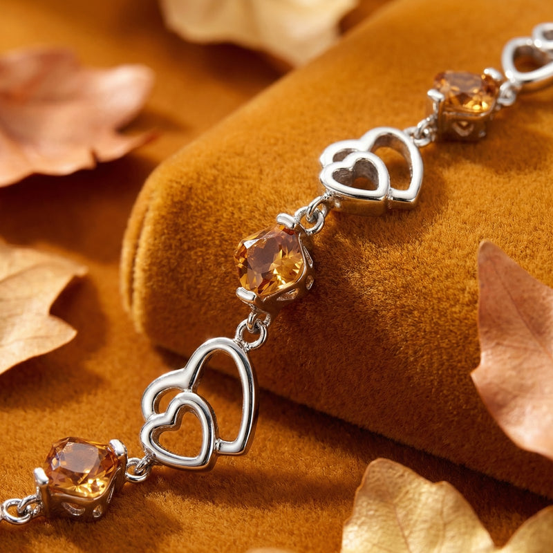 Macro view of square-cut simulated topaz stones and silver heart links on the Amantelle sterling silver bracelet.