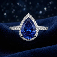Pear-cut simulated sapphire halo ring in solid gold on a blue velvet background.