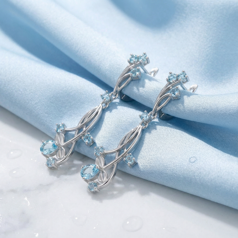 Side view of sterling silver Lyriane drop earrings featuring light blue simulated aquamarine on blue fabric.