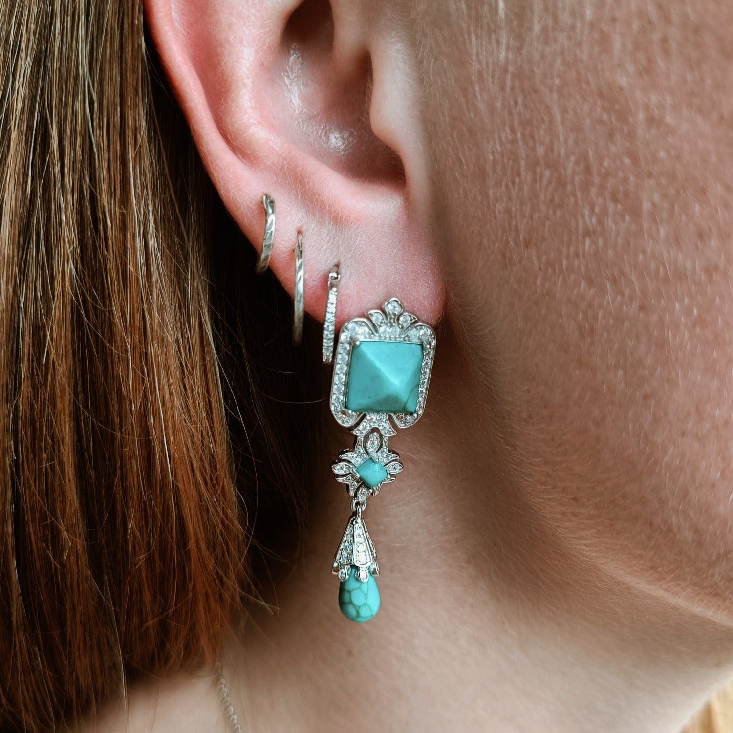 Turquoise Seabed Earrings featuring turquoise stones in a sterling silver setting on a model left ear zoom