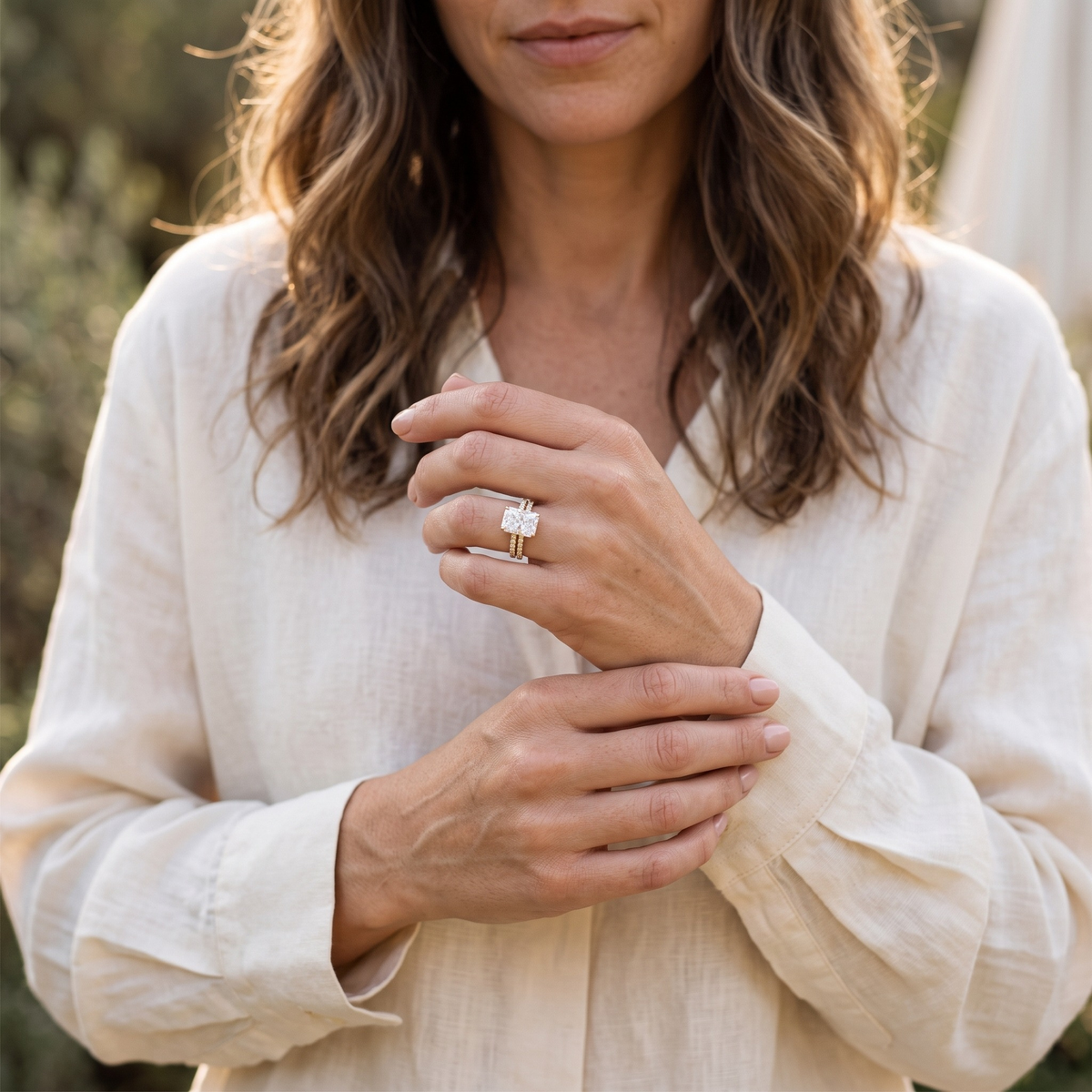 Yellow-gold radiant-cut moissanite ring set worn on a model's hand near her cuff.