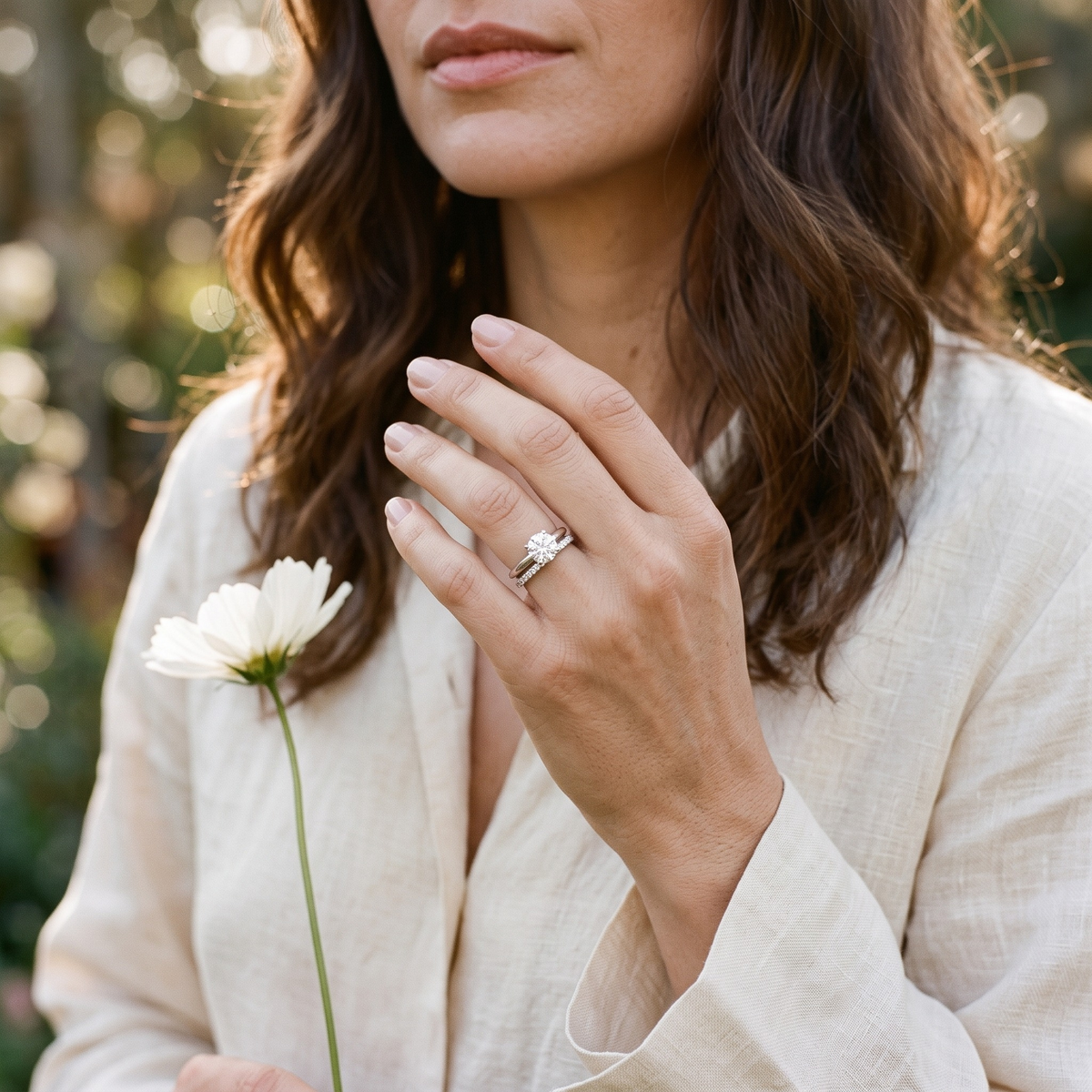Silver round-cut moissanite ring set worn on a model's hand holding a flower.