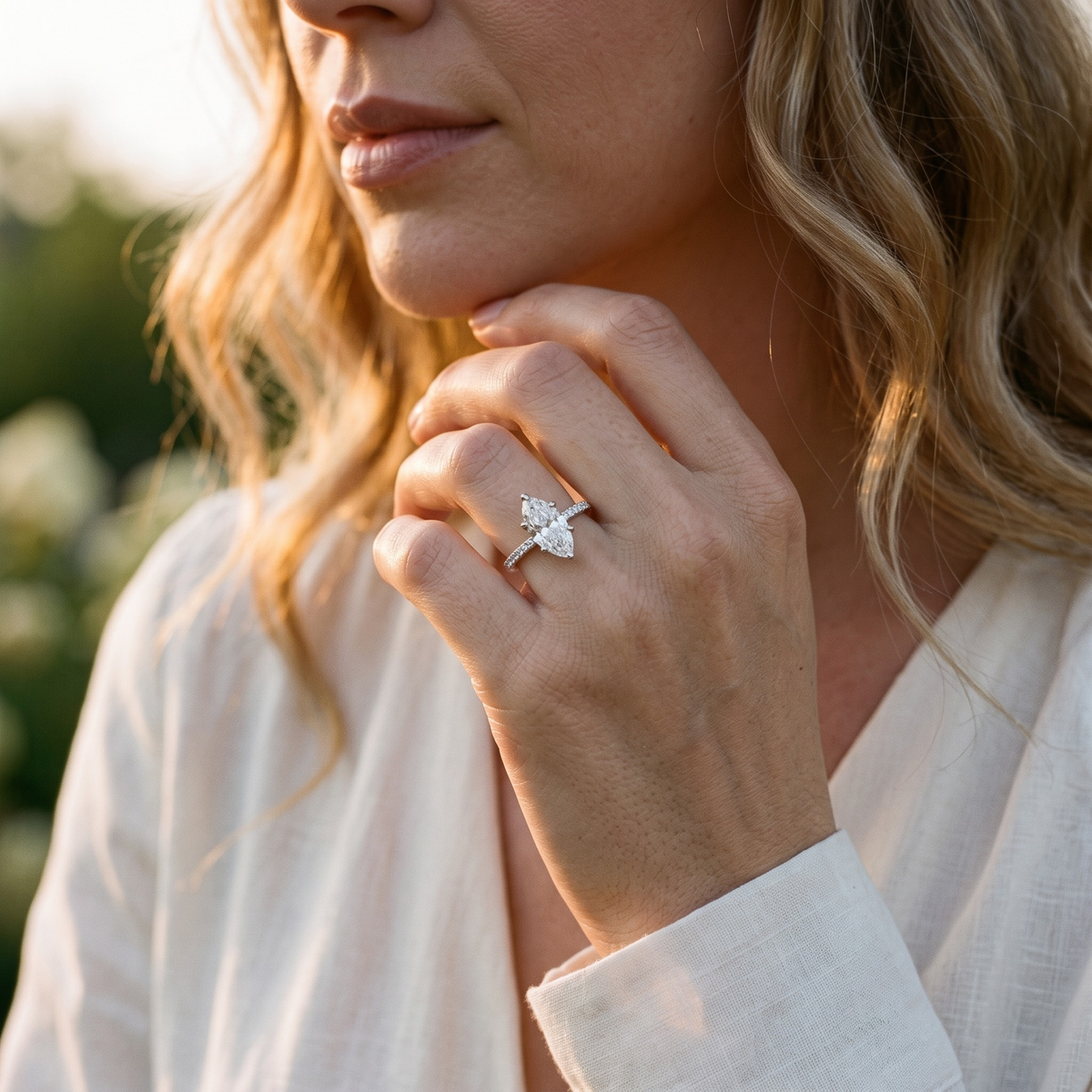 Silver marquise moissanite ring worn on a model's hand near her chin.