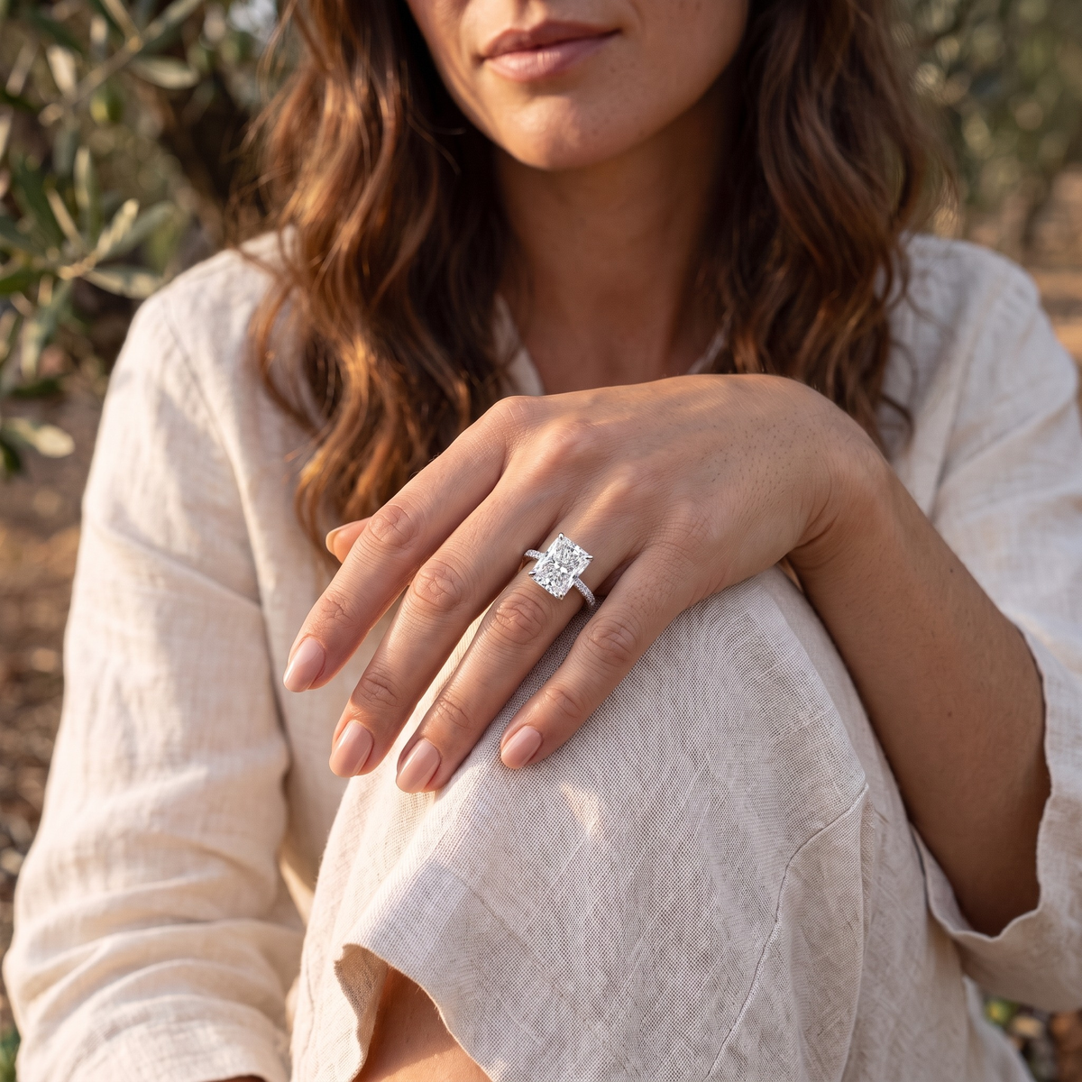 Silver radiant-cut moissanite ring worn on a model's hand resting on her knee.