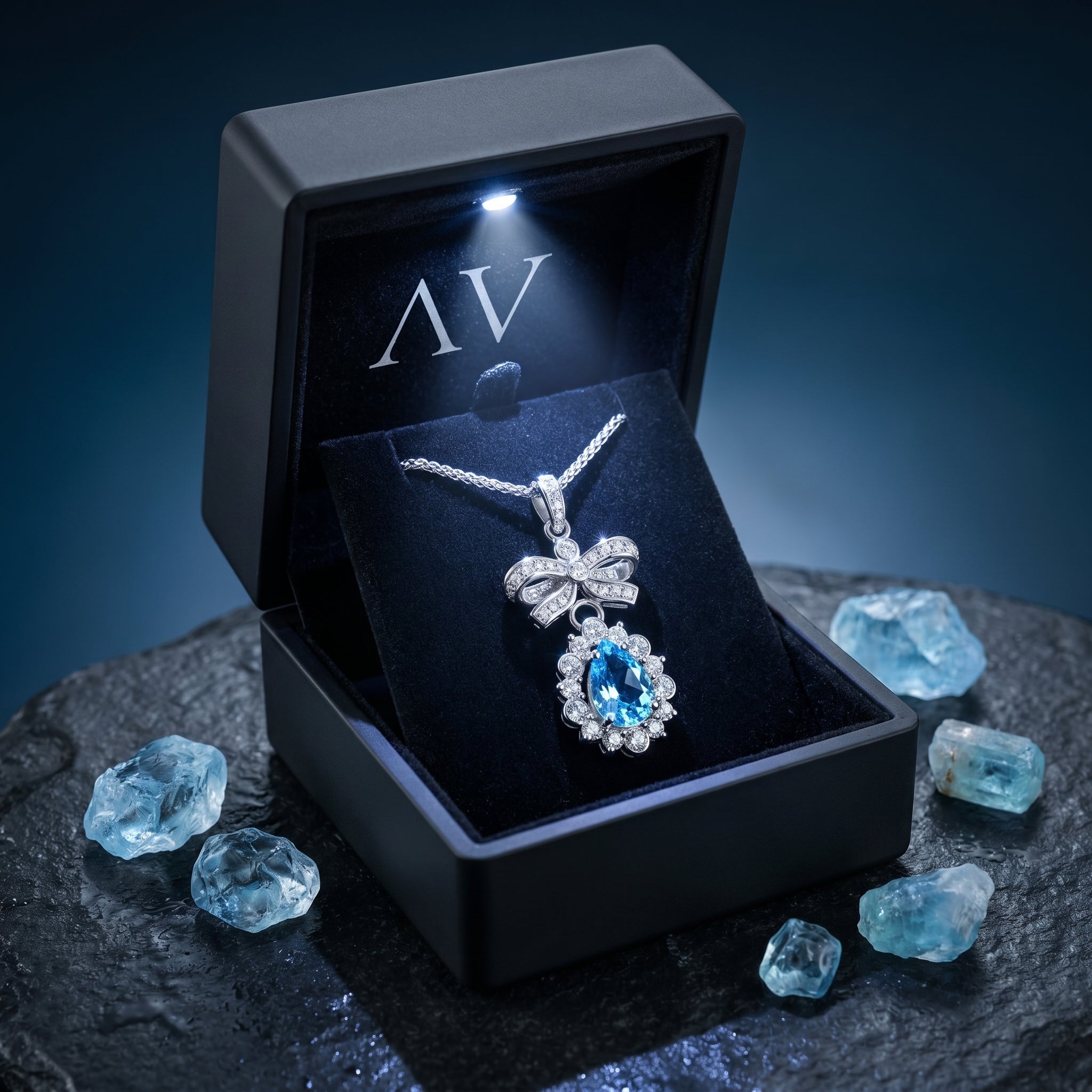 Silver pear cut aquamarine bow necklace presented in a lighted black gift box surrounded by raw blue gemstones.
