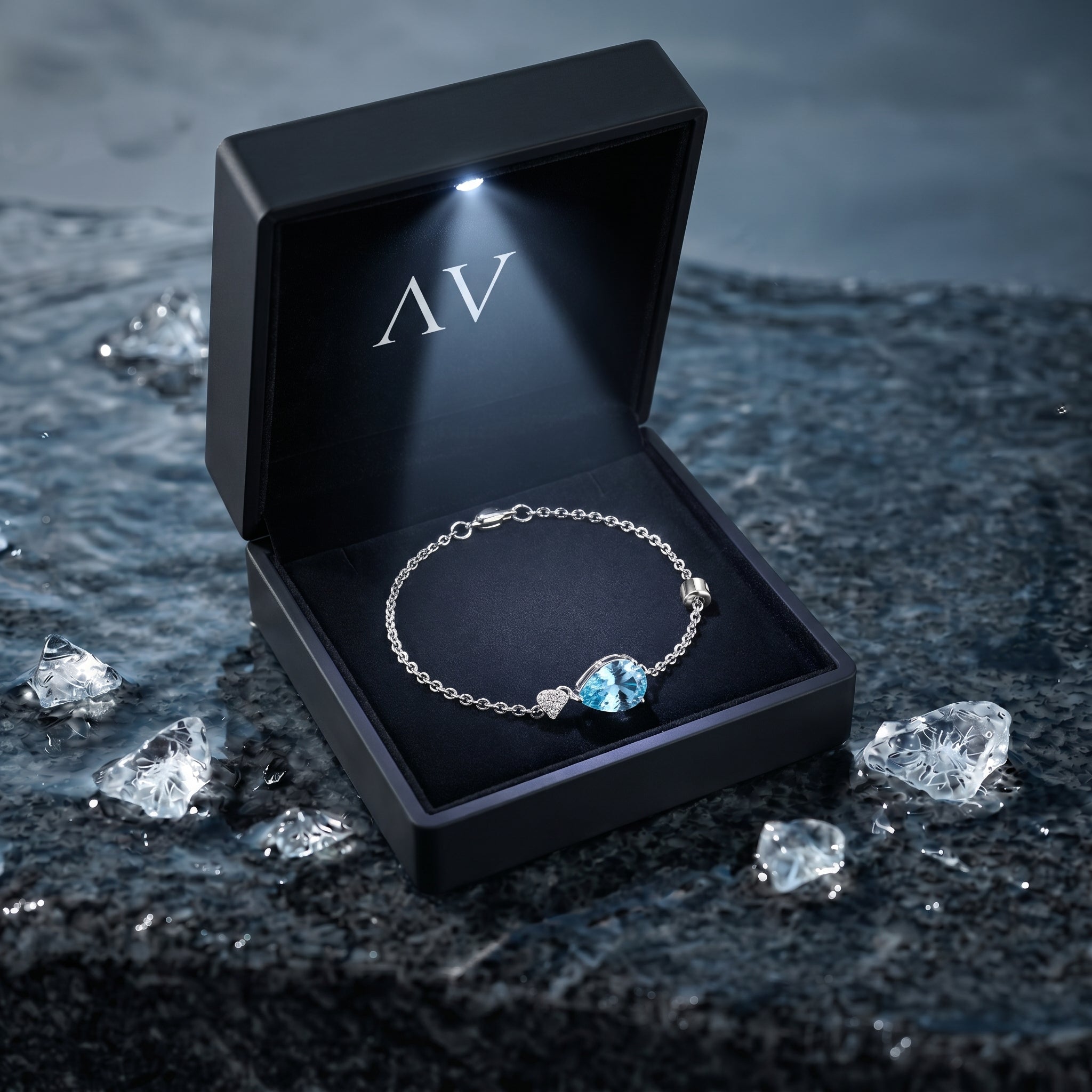 Pear-cut aquamarine platinum bracelet inside a lighted black gift box on a wet stone surface.