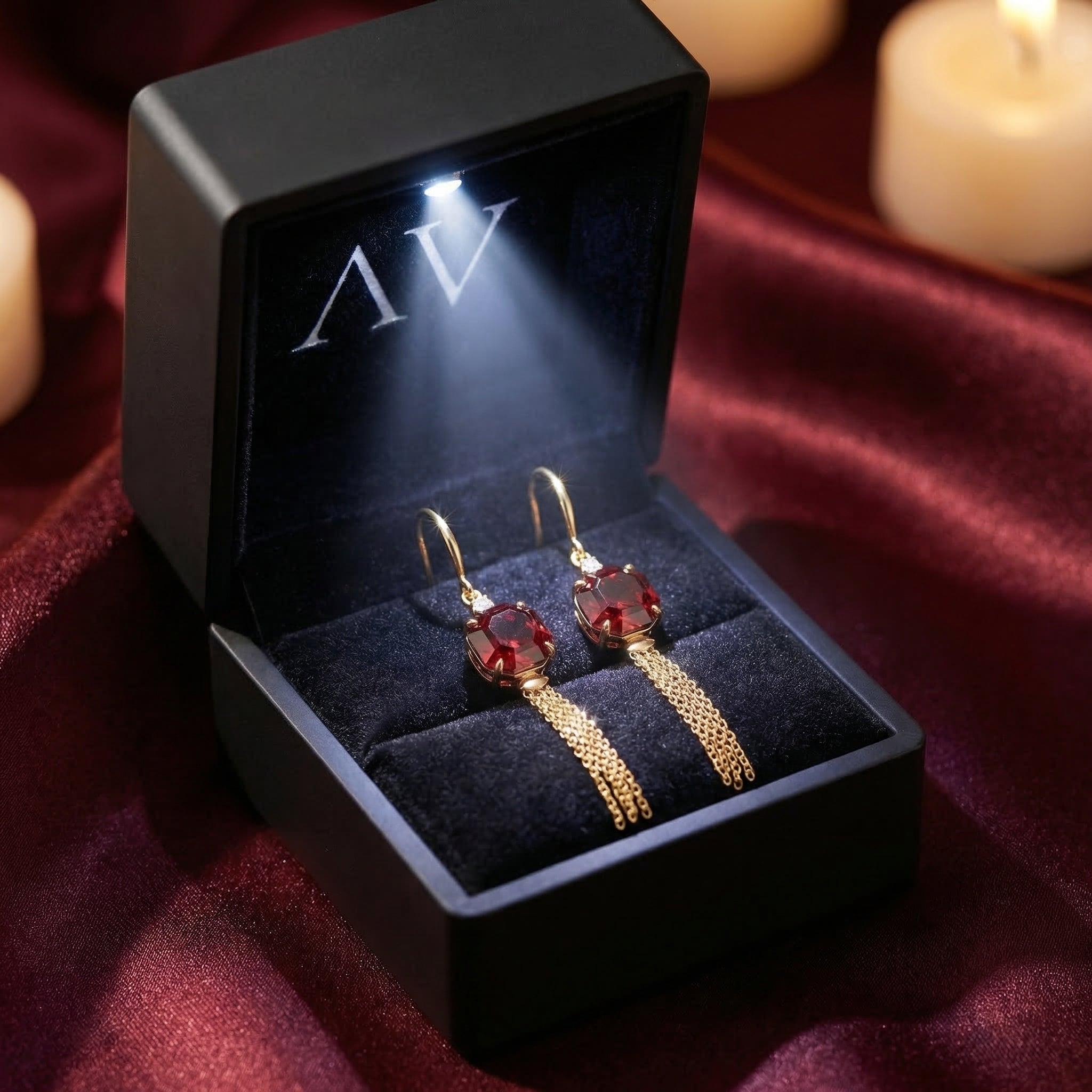 18K yellow gold garnet drop earrings displayed in a black illuminated jewelry box on red fabric.