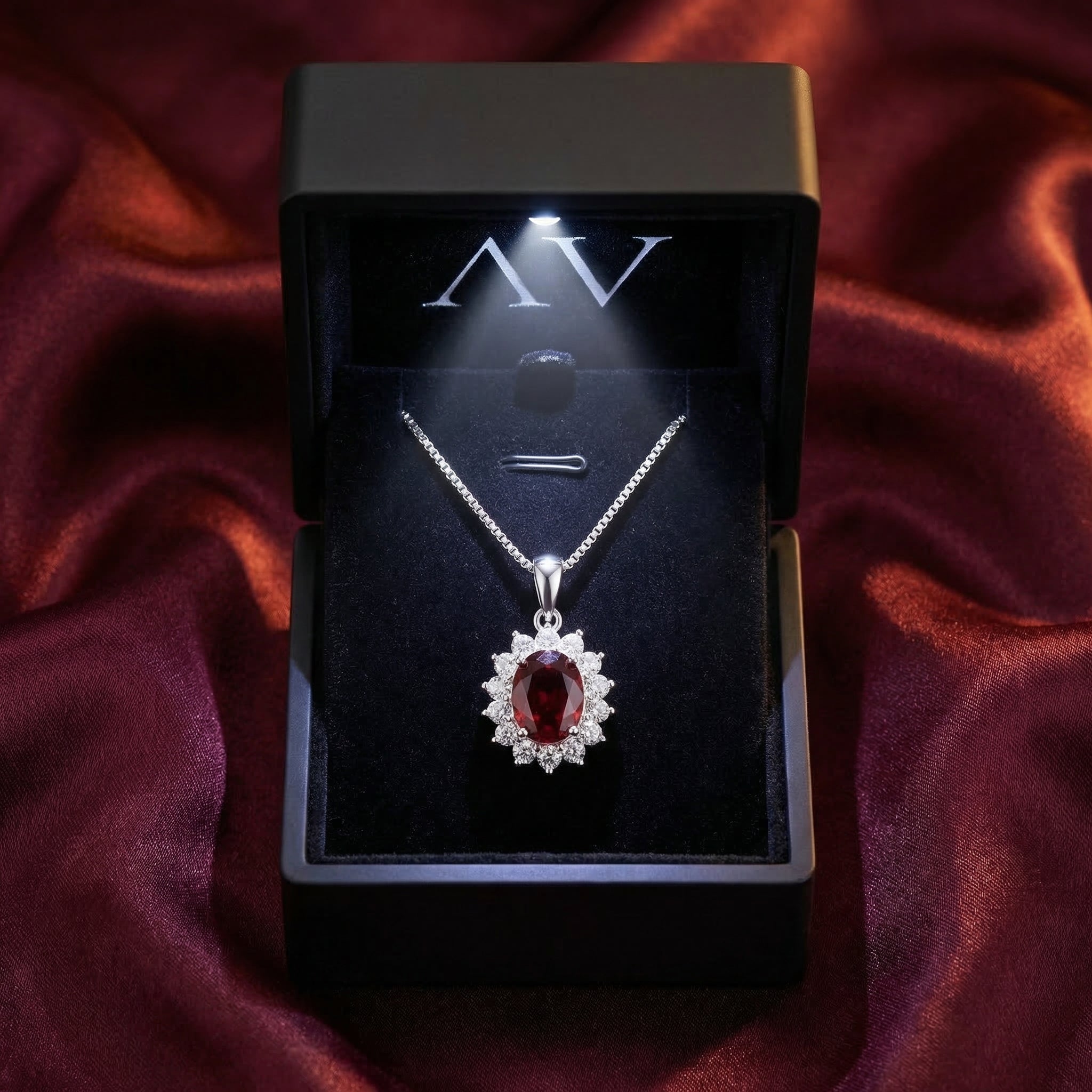 The Odilia silver oval garnet necklace presented in a lighted black jewelry box on burgundy silk.