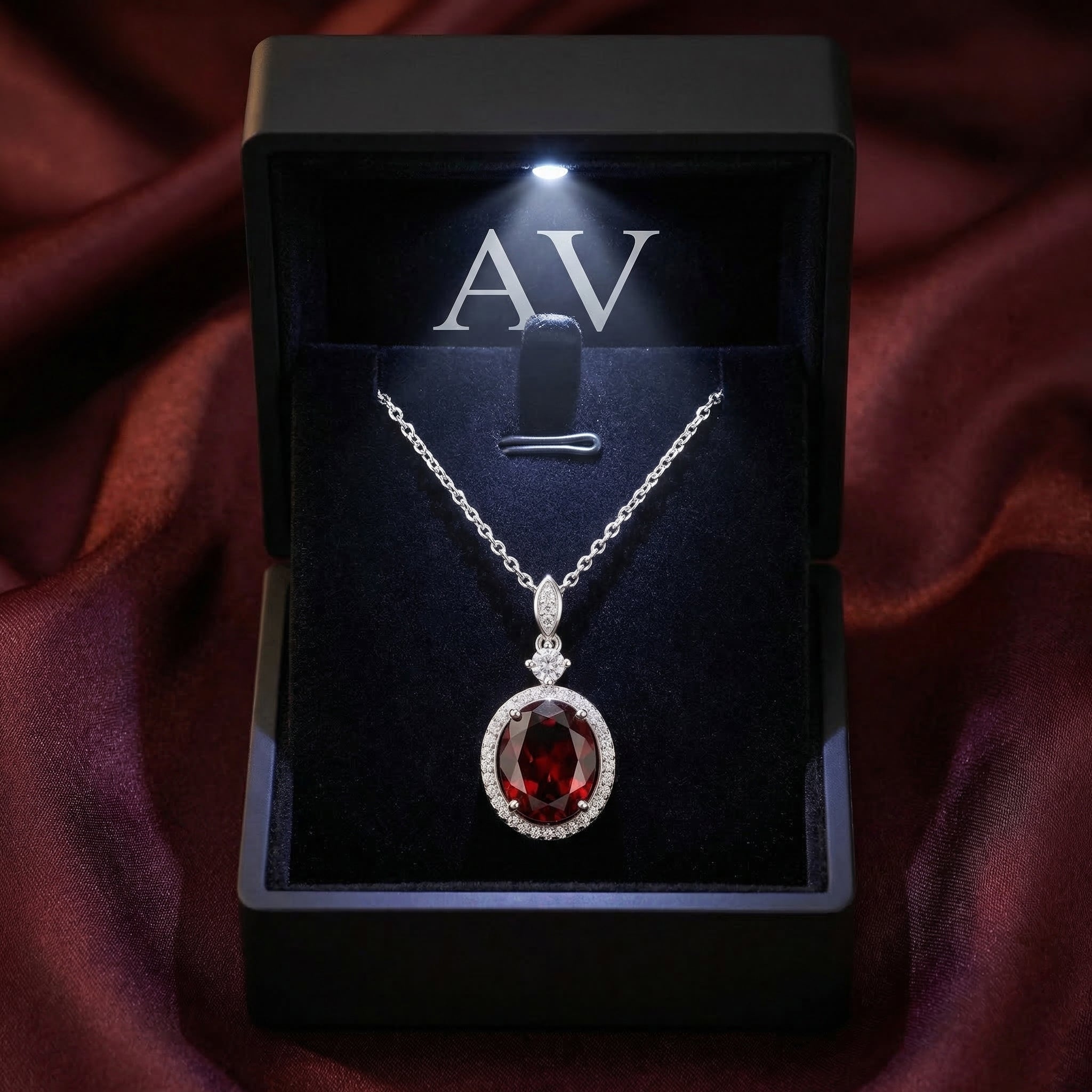 The Kaelia oval garnet necklace presented in a premium black LED-lit gift box on burgundy fabric.