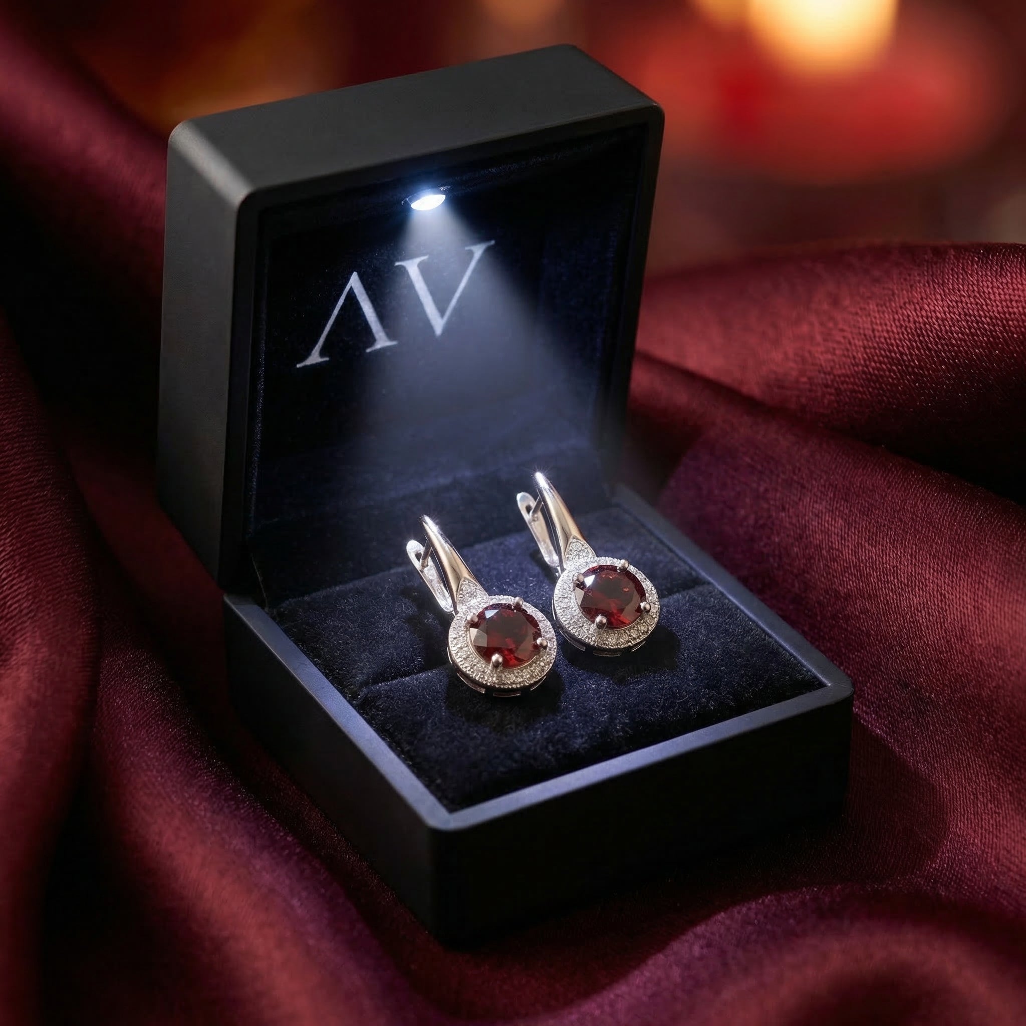 Garnet drop earrings presented in a black LED-lighted jewelry box on burgundy silk fabric.