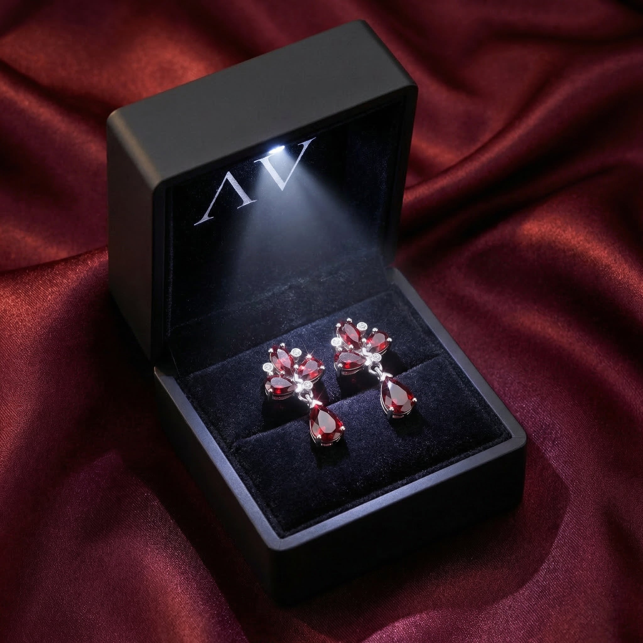 Fiamma cluster garnet earrings in a lighted black gift box resting on burgundy silk fabric.