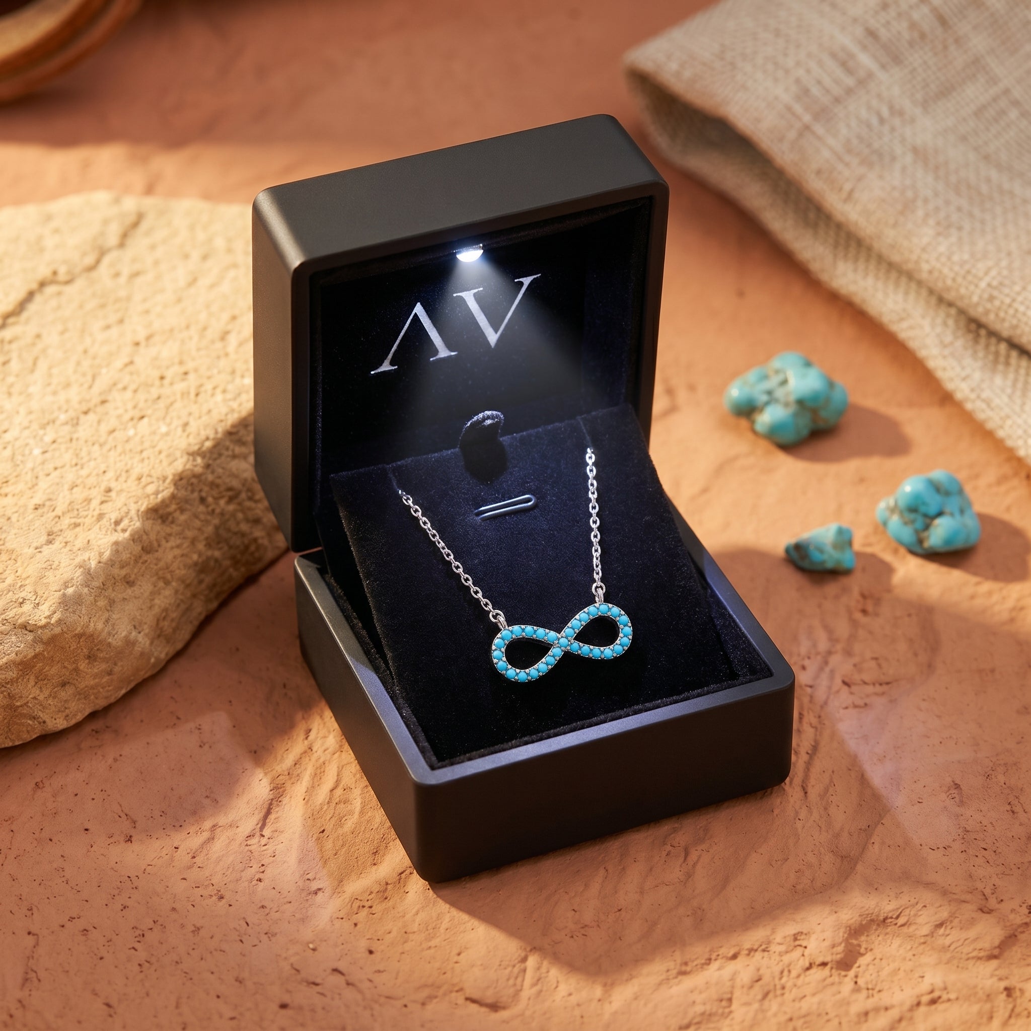 Silver infinity turquoise necklace presented in a black LED-lit gift box on a desert-inspired background.