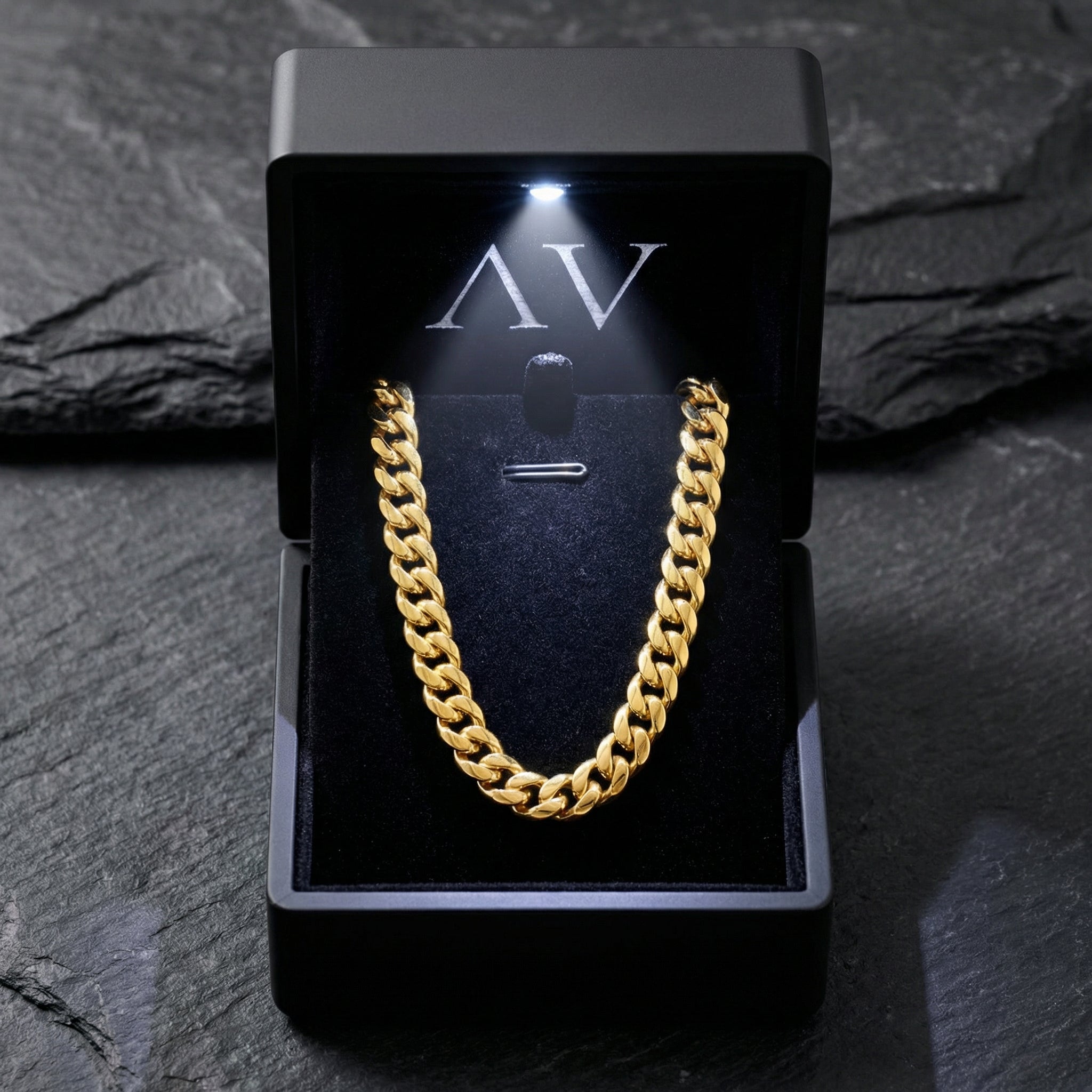 Gold stainless steel Cuban link chain inside a black LED-lit jewelry box on a dark stone surface.