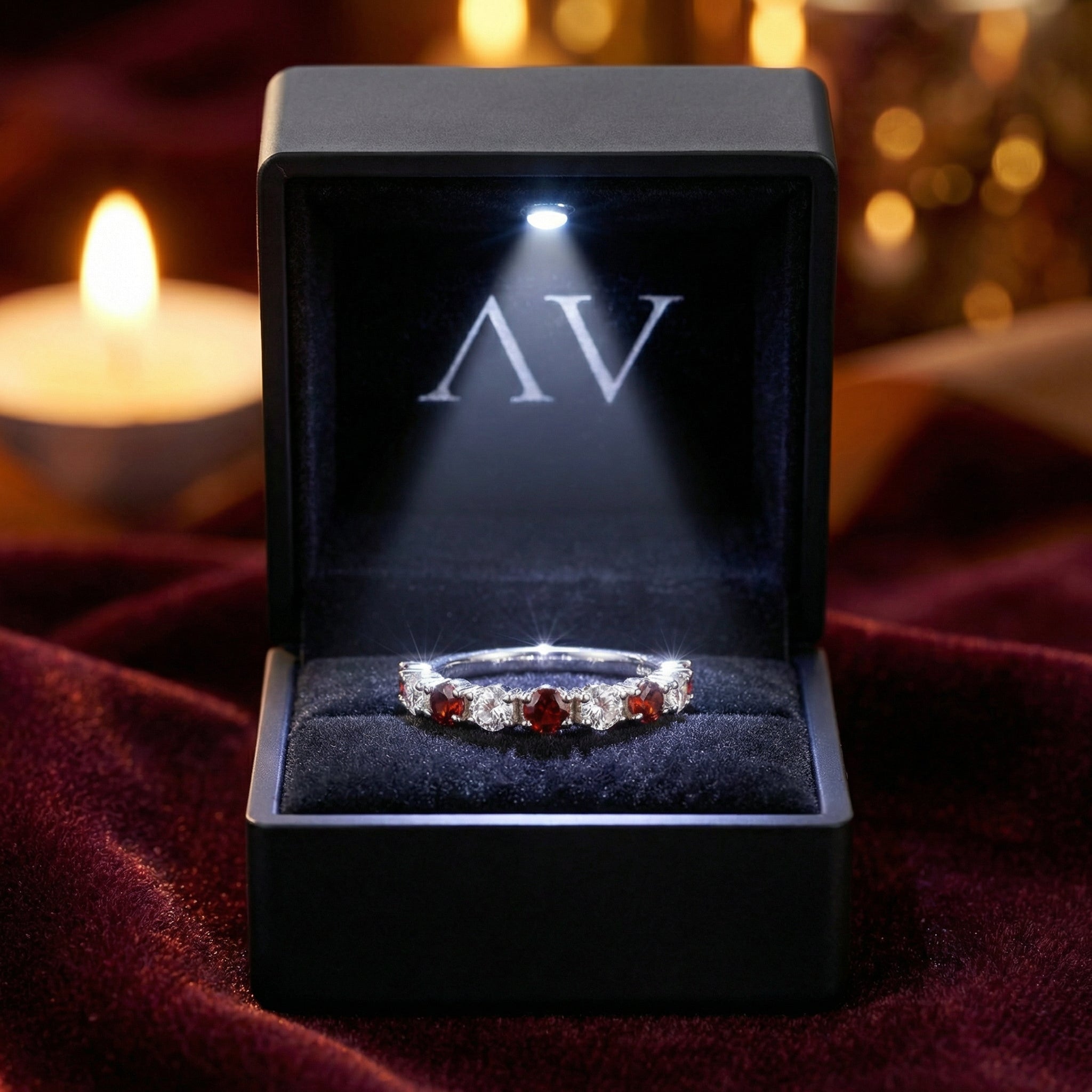Aeliana eternity ring with red simulated garnets in a lighted black AV branded jewelry presentation box.