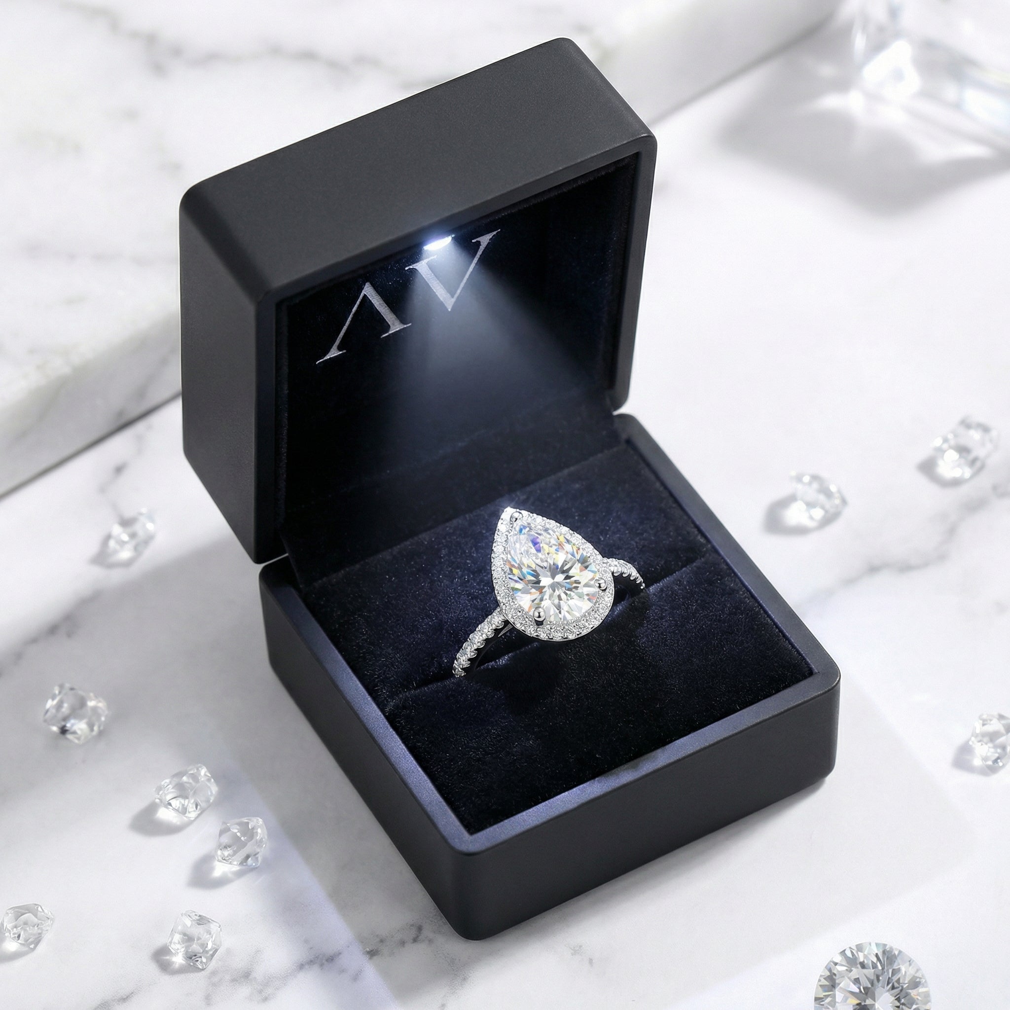 Pear-cut simulated diamond halo ring in a black LED-lit jewelry box on a marble surface.