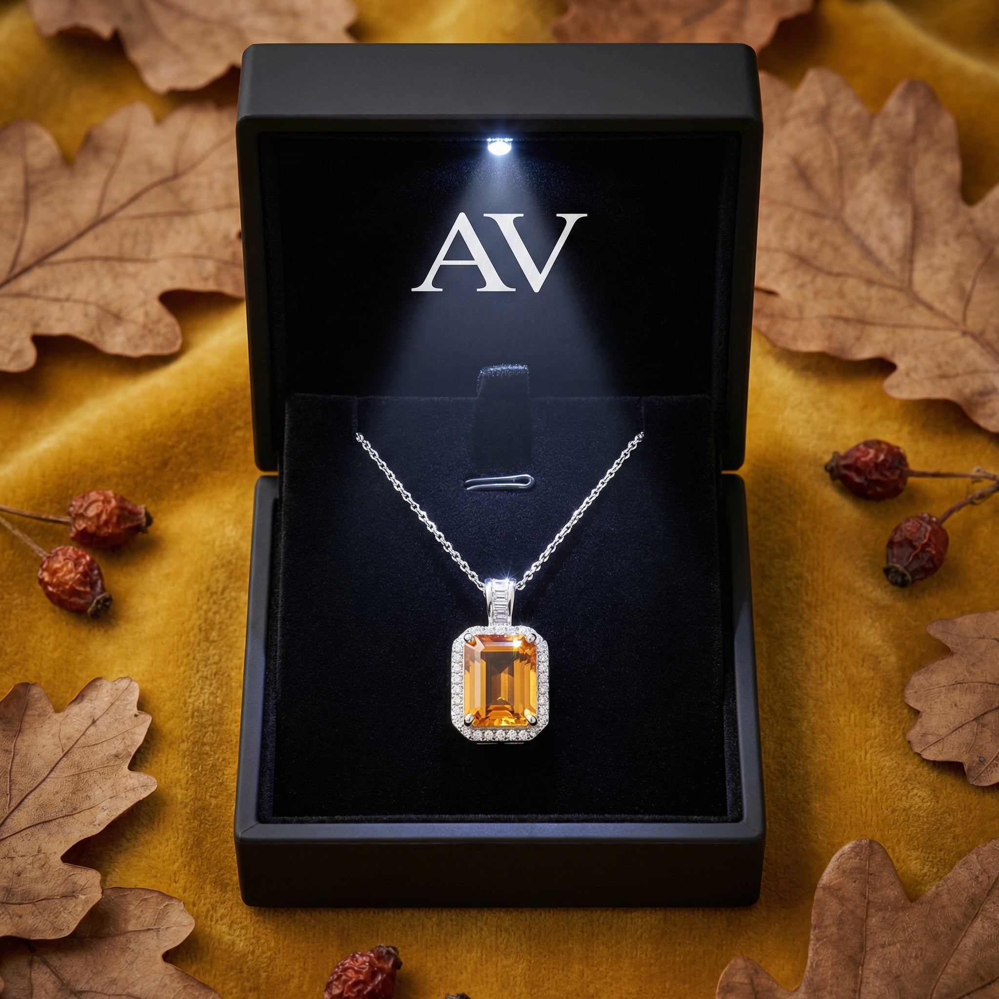 Emerald cut simulated topaz necklace in a lighted black gift box surrounded by autumn leaves.