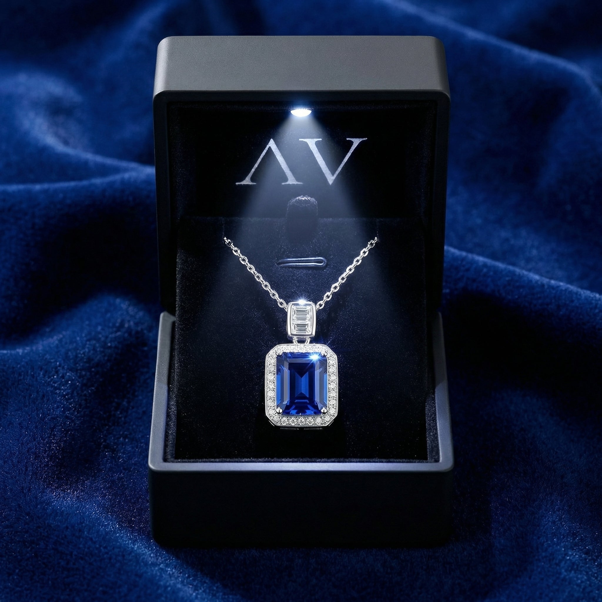Emerald cut blue sapphire pendant necklace presented in a black lighted jewelry gift box on blue velvet.