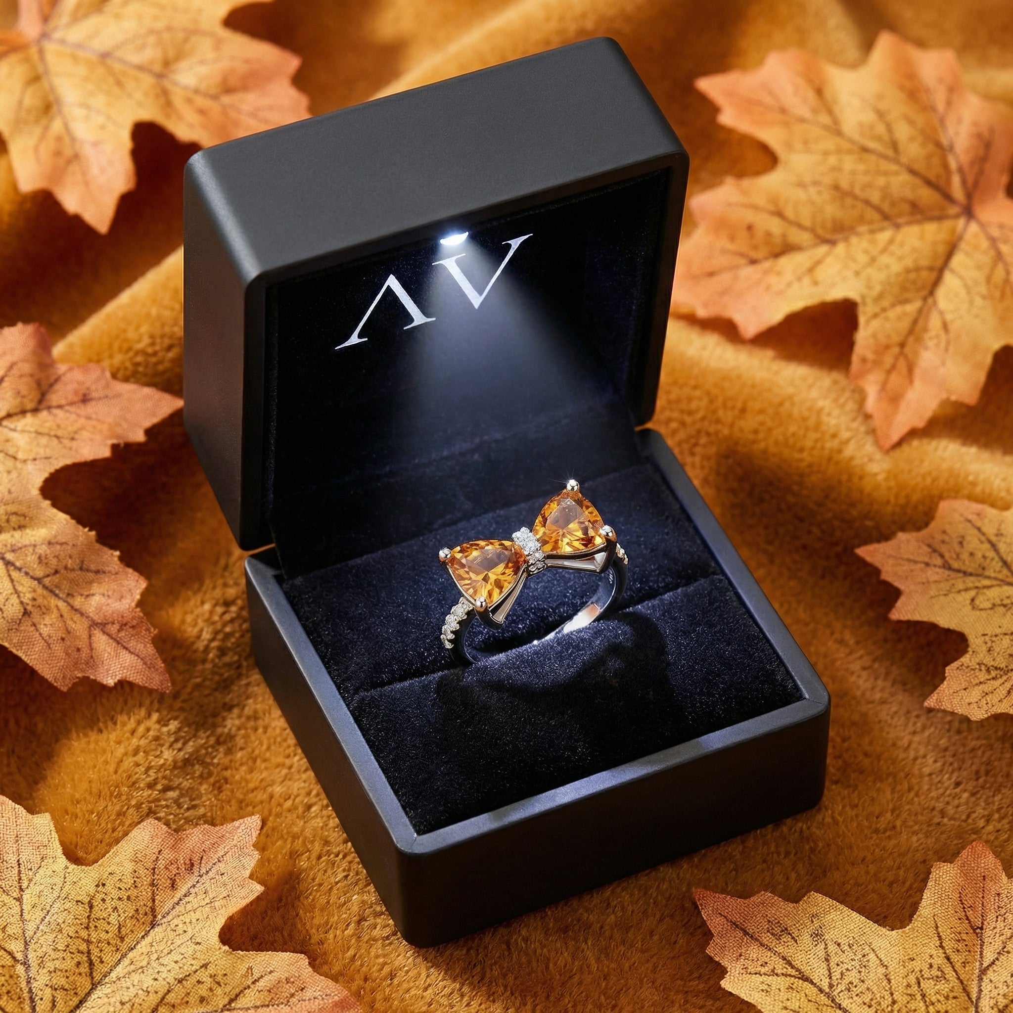 Sterling silver honey topaz bow ring inside a black LED-lit gift box surrounded by autumn leaves.