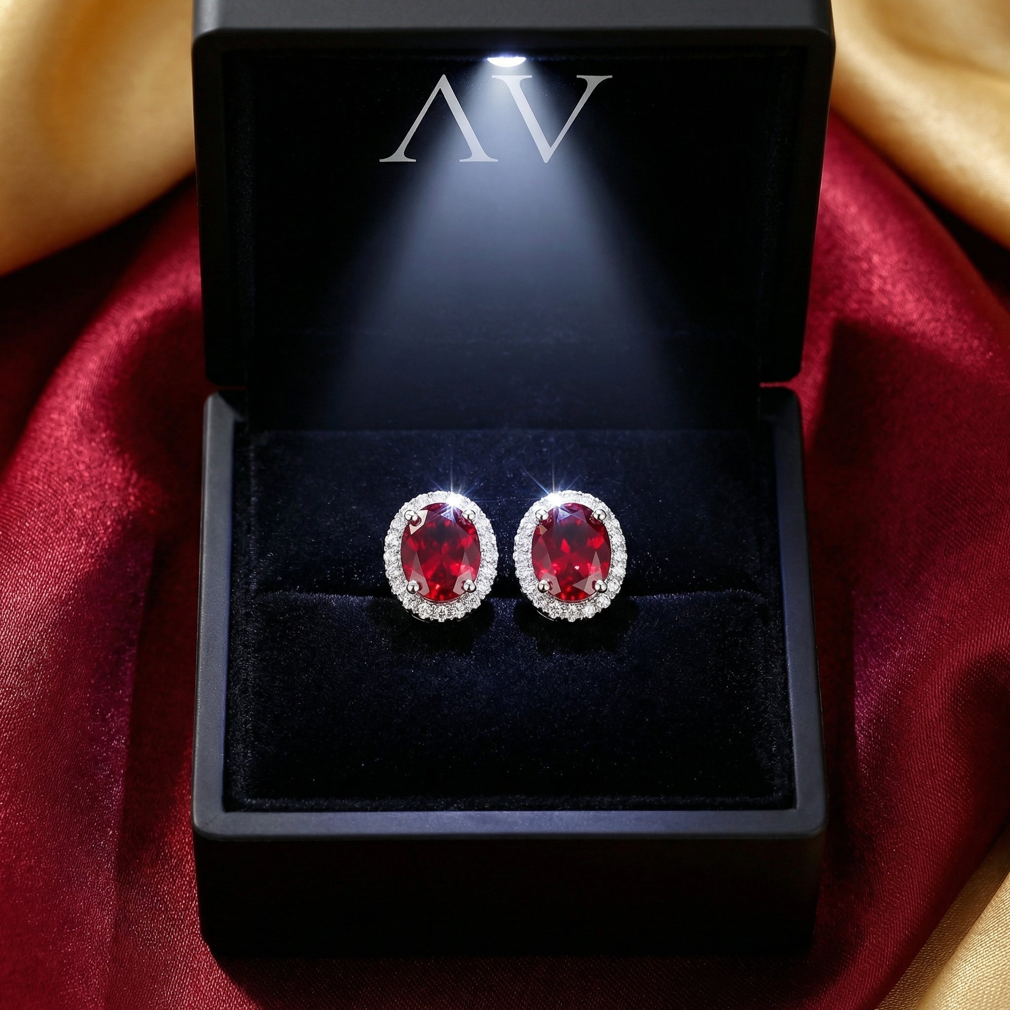 Oval simulated ruby halo stud earrings in S925 sterling silver inside a black LED-lit gift box.