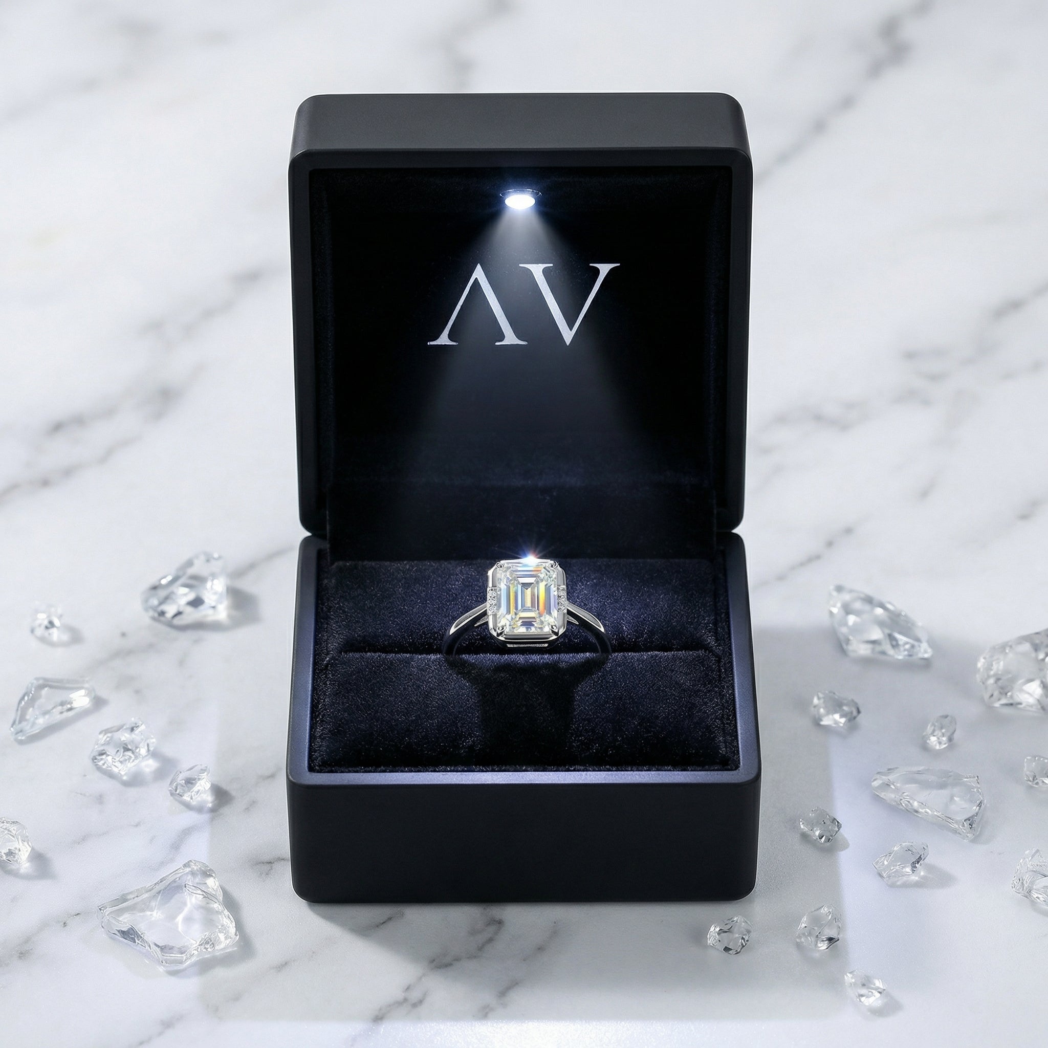 Emerald-cut moissanite ring presented in a black LED-lit jewelry box on a marble background.