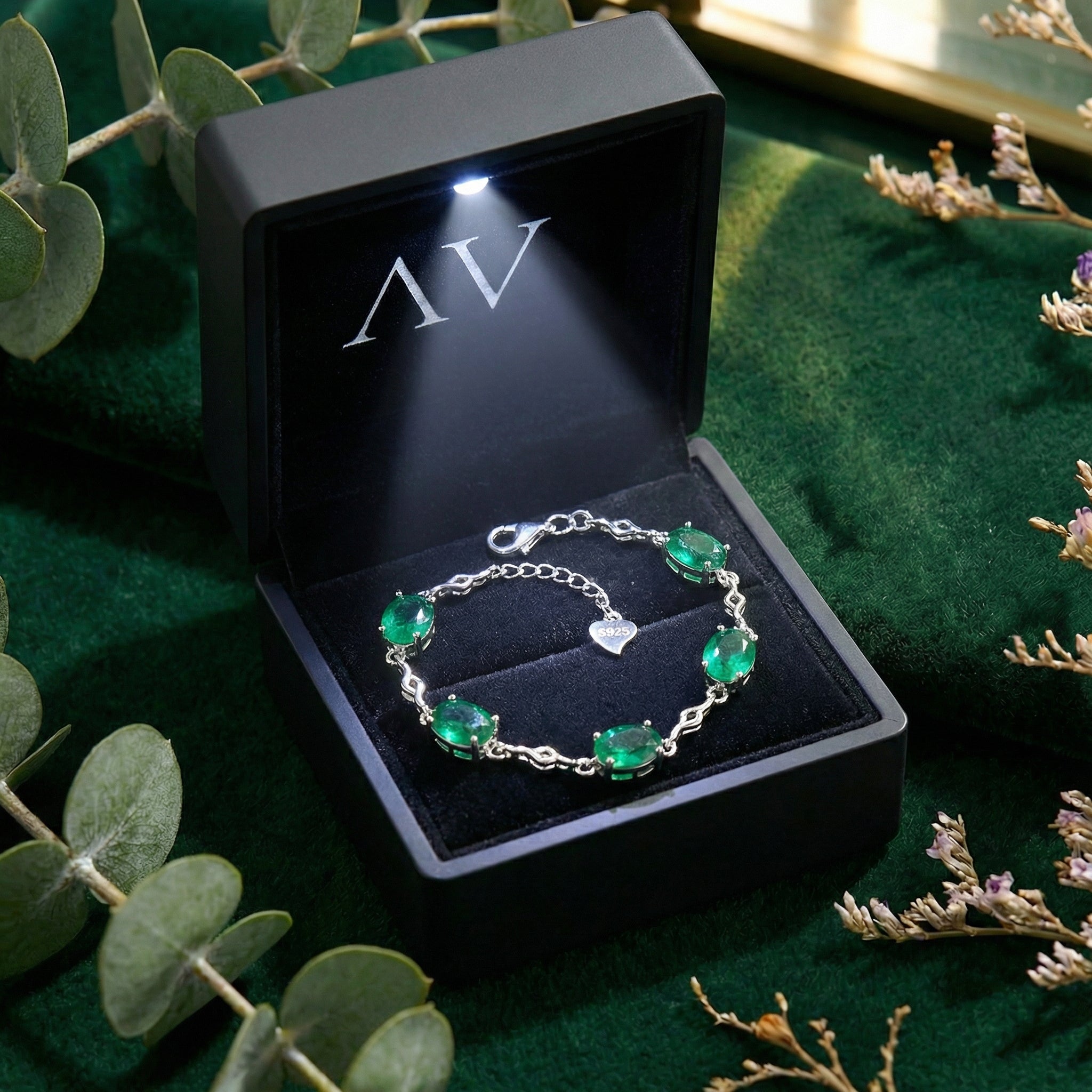 Simulated emerald station bracelet in a black LED-lighted jewelry box on a green velvet surface.