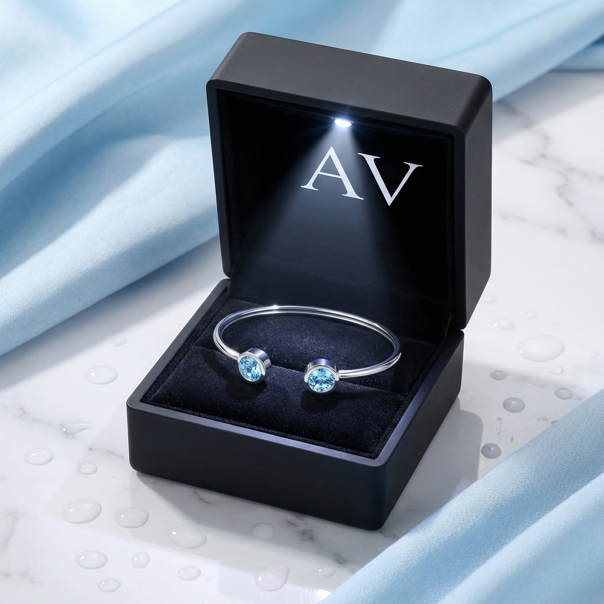 Silver stainless steel Cyrene bangle with round-cut simulated aquamarine stones in a lighted black jewelry box.