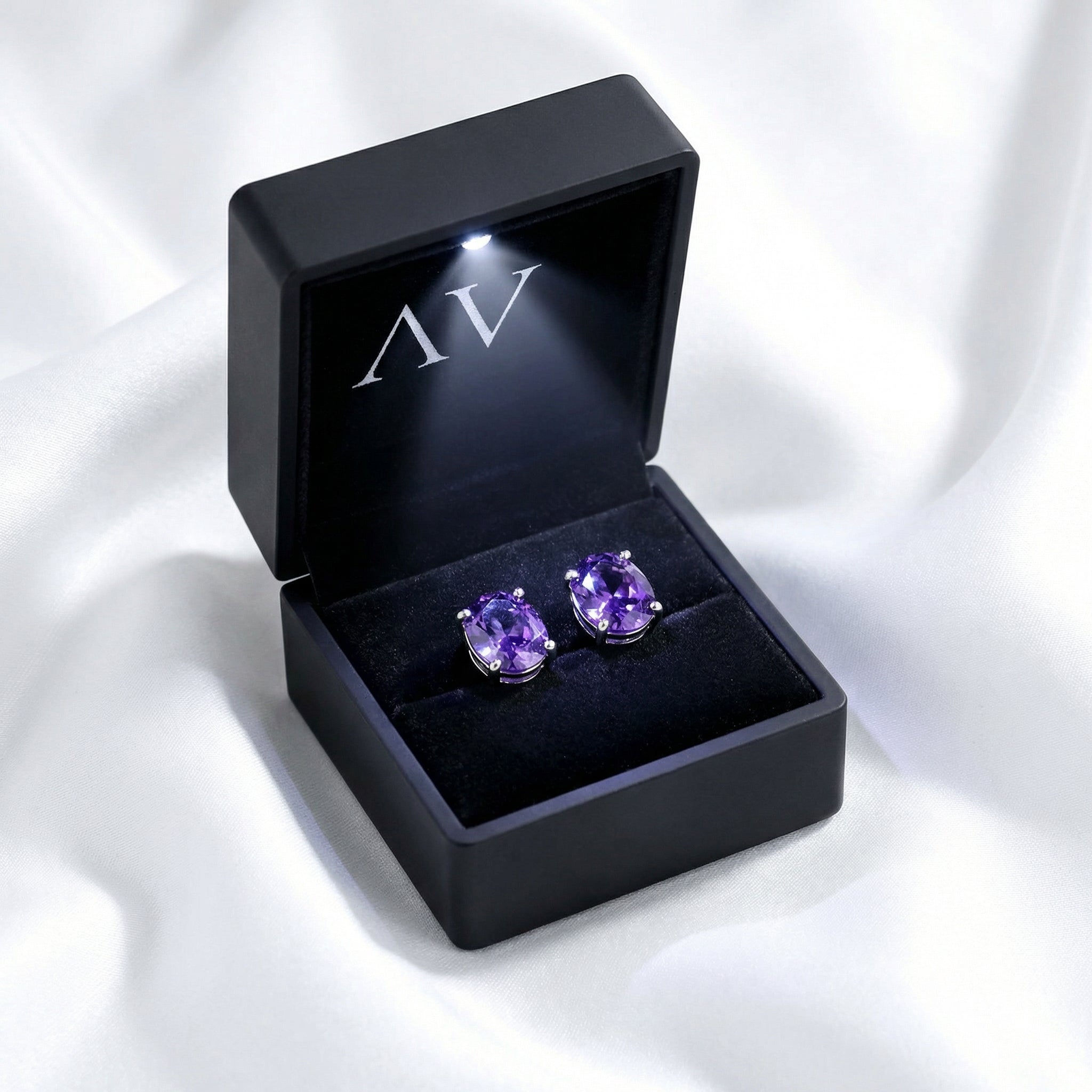Pair of oval cut purple simulated amethyst stud earrings inside a black LED-lighted jewelry box.