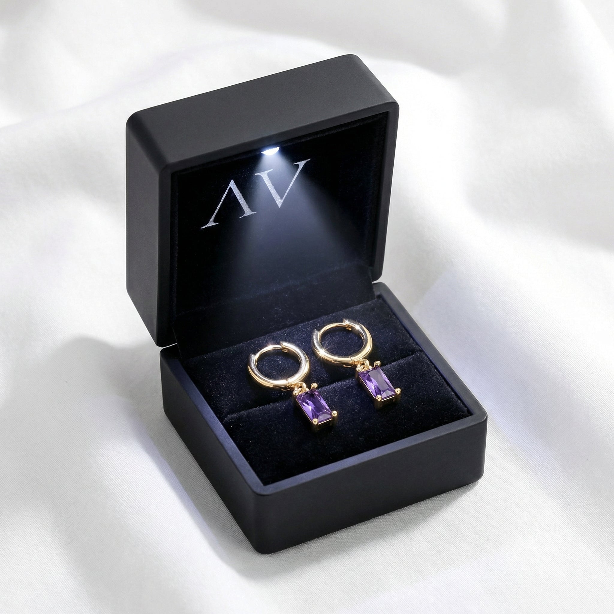 Gold Vivienne drop earrings with purple stones inside a black LED-lit jewelry presentation box.