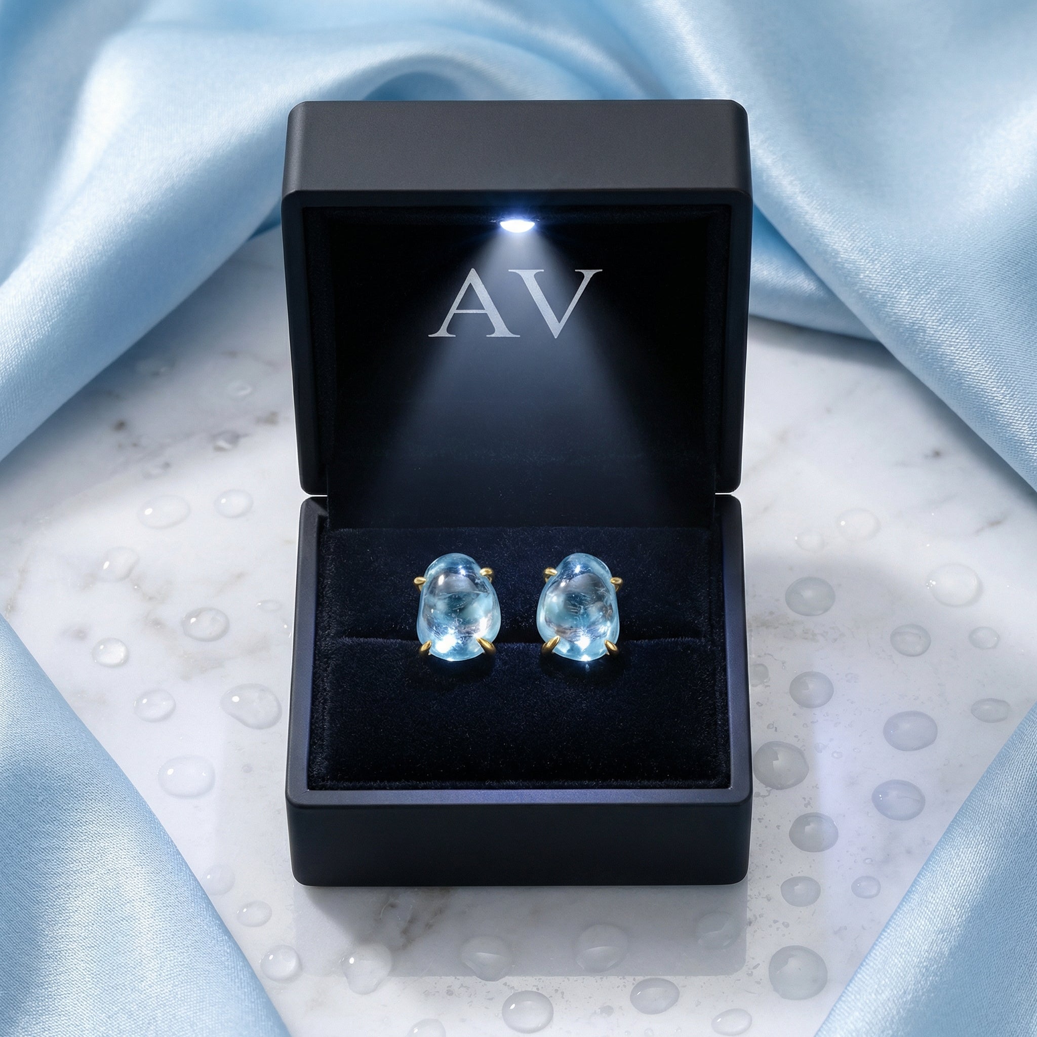 Organic cut March birthstone simulated aquamarine stud earrings in 18K gold vermeil inside a black LED-lit box.