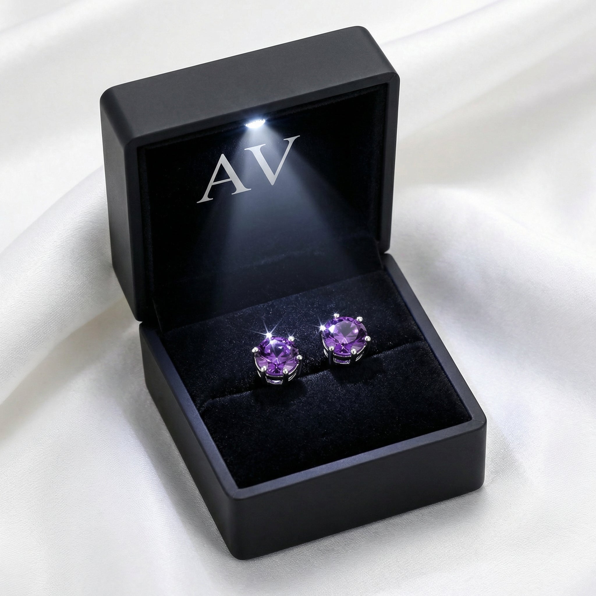 Round cut simulated amethyst studs in a black LED-lit jewelry presentation box on white silk.