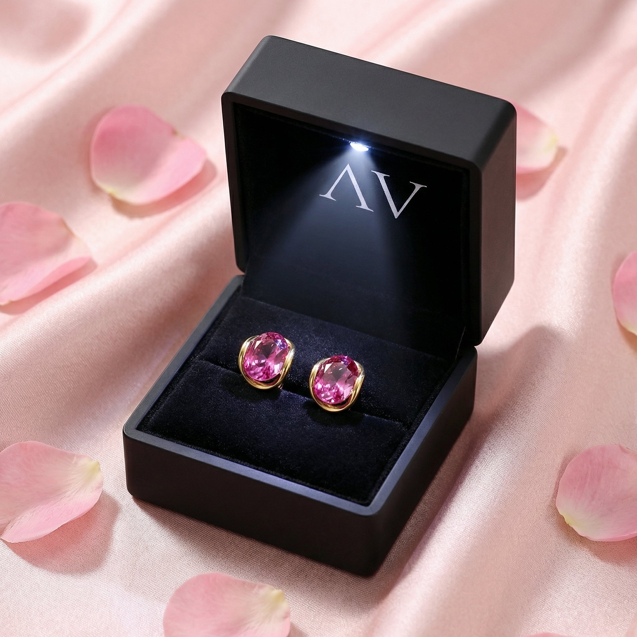 Pair of oval pink tourmaline gold earrings inside a black lighted jewelry gift box on pink silk.