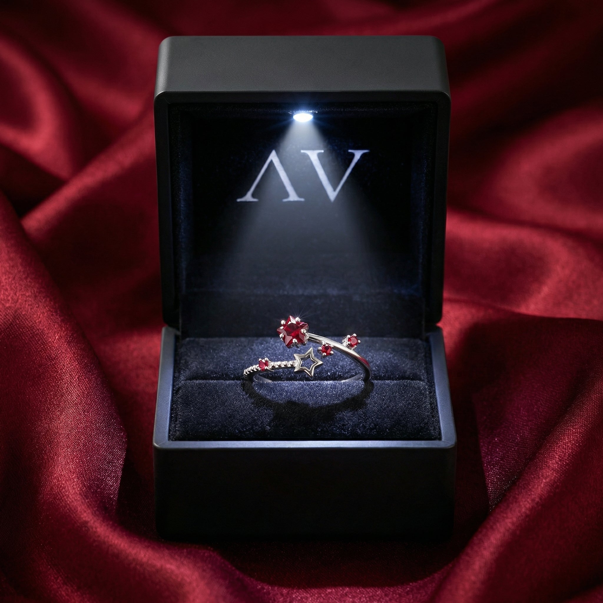 Lyriana star ring with red simulated rubies presented in a black LED-lit jewelry box on red silk.