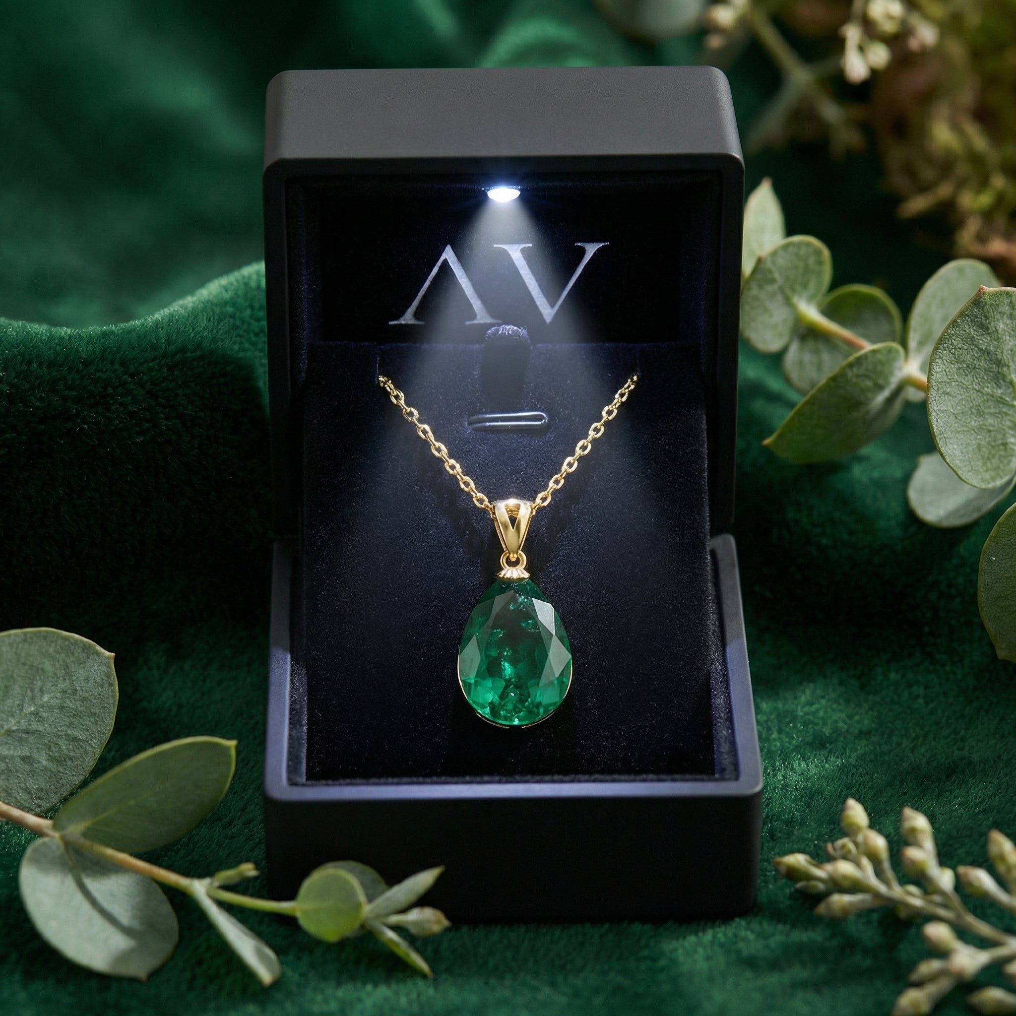 Pear-cut simulated emerald gold necklace inside a black LED-lit jewelry gift box on a green velvet surface.