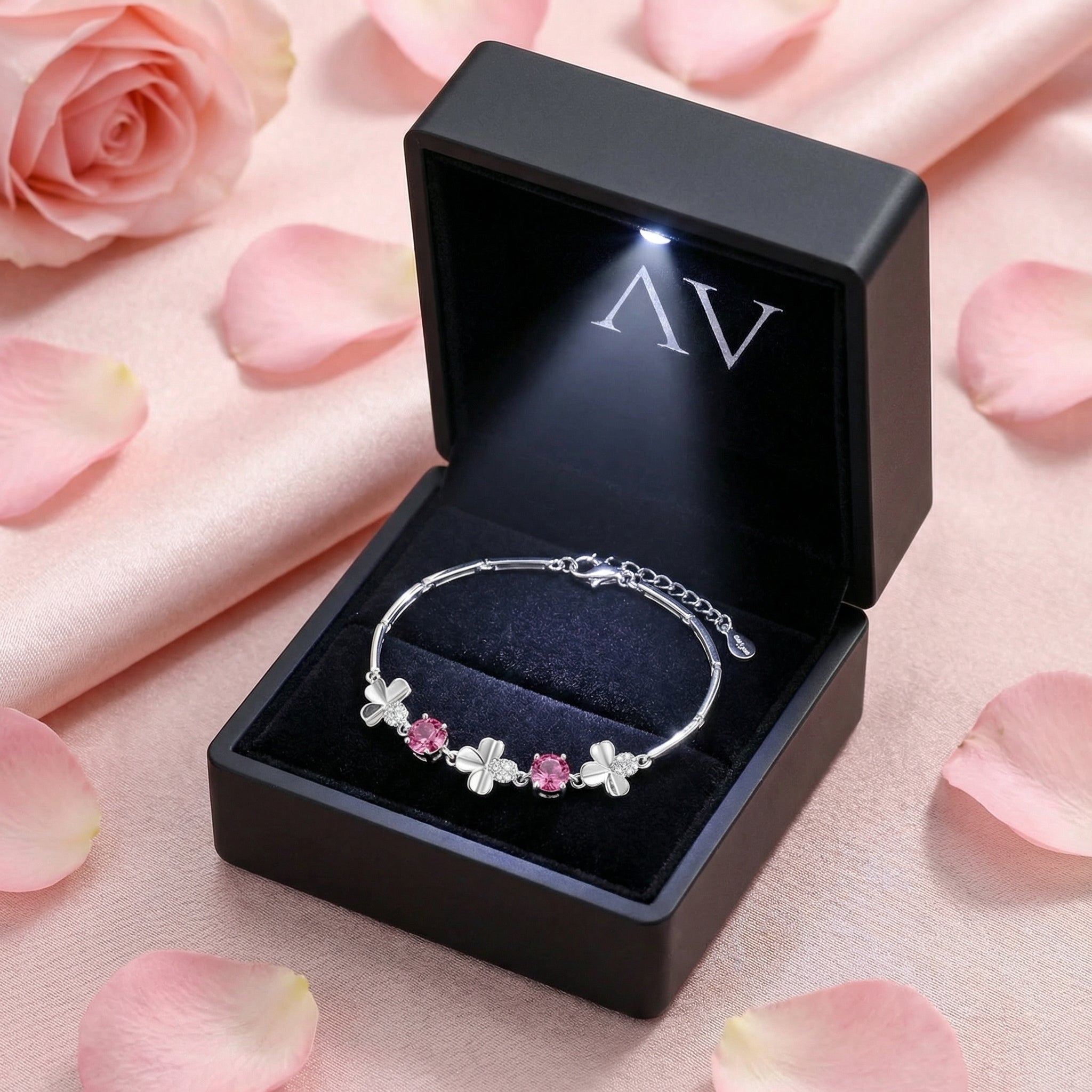 Sterling silver pink tourmaline clover bracelet in a black LED-lit gift box with rose petals.