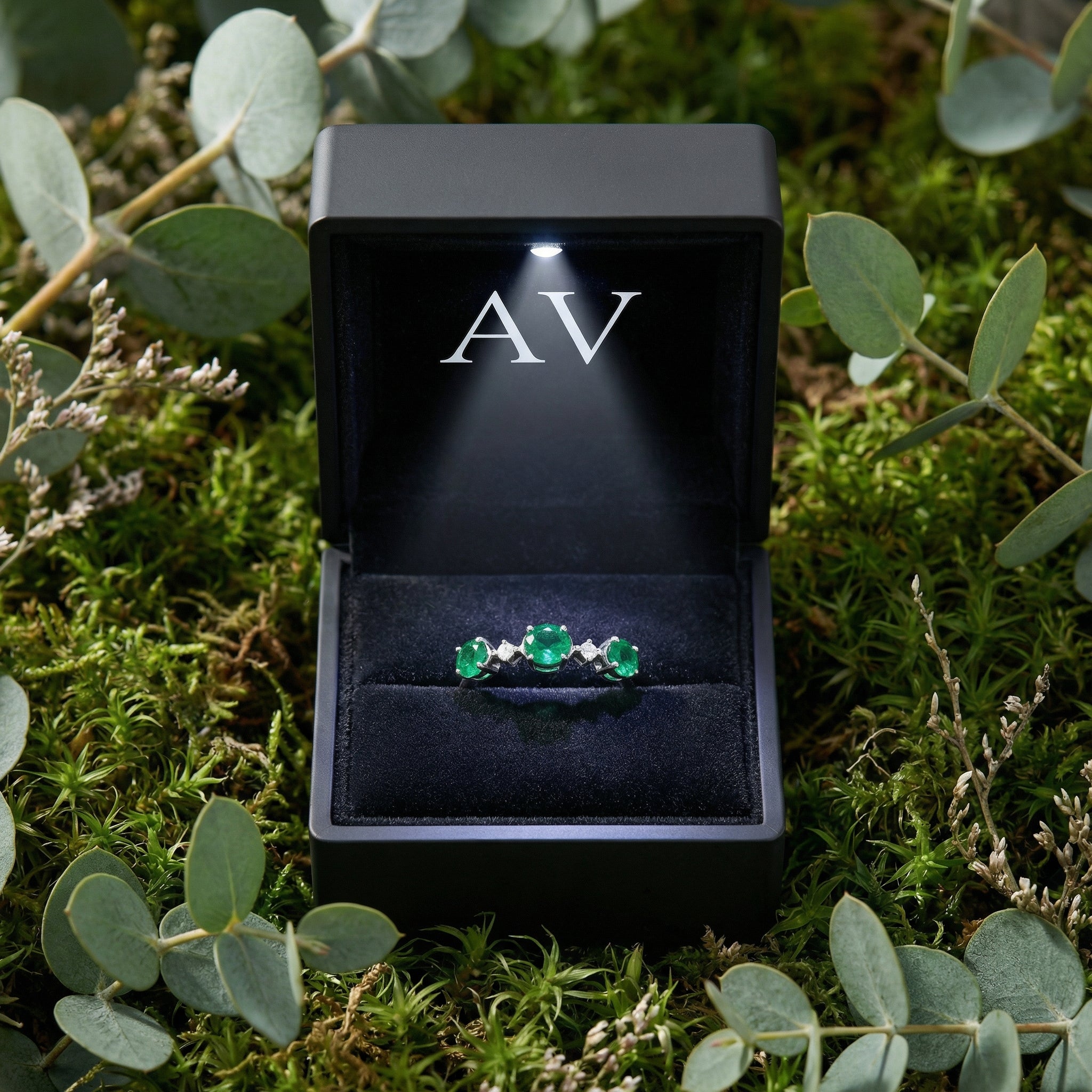 Front view of the sterling silver bypass ring with three oval simulated emeralds in an open black presentation box.