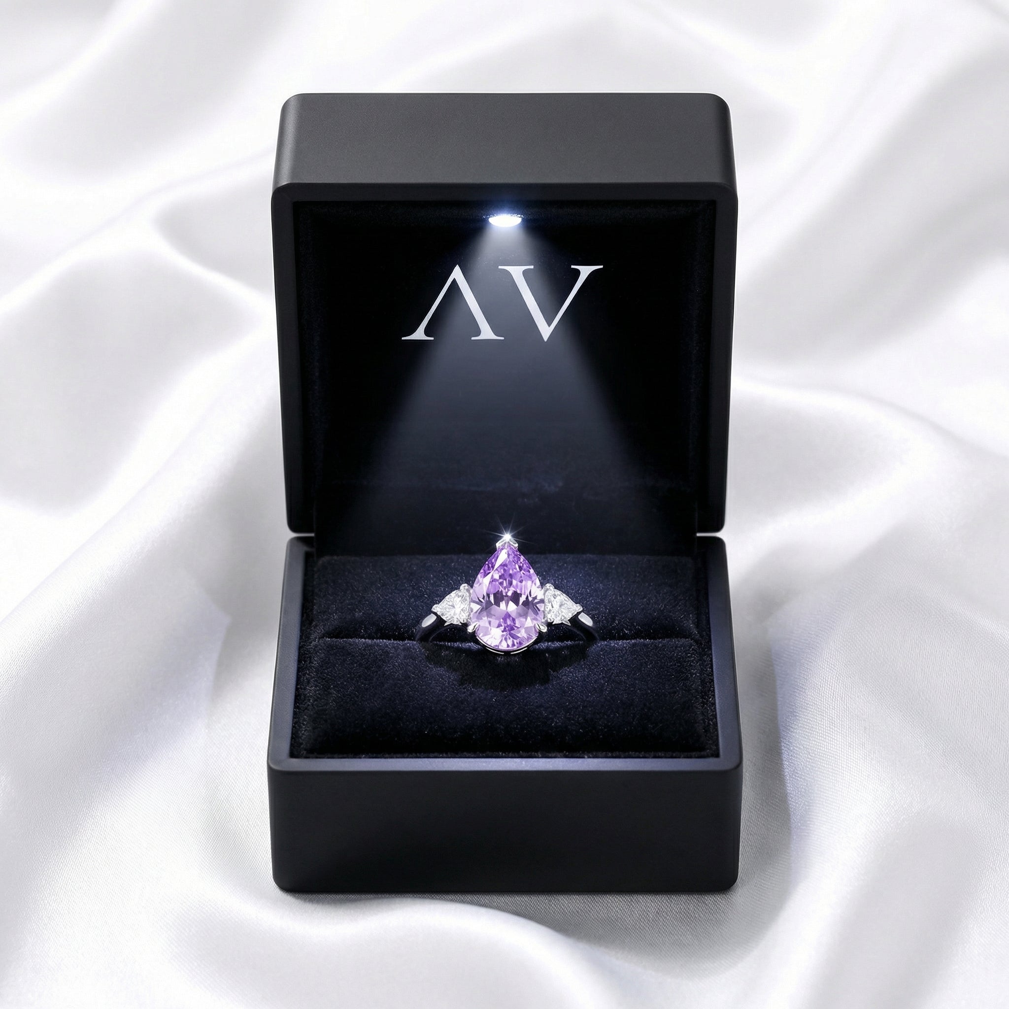 Pear-cut royal purple simulated amethyst ring in a black LED-lighted jewelry box on white silk.