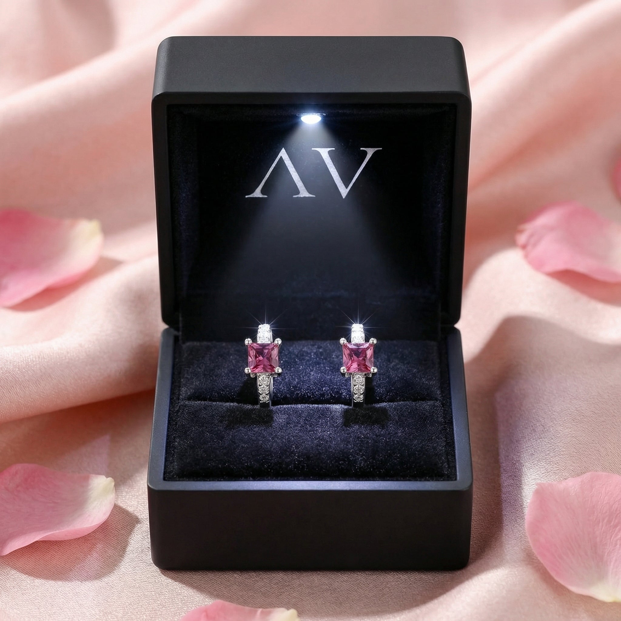 Pink tourmaline square huggie earrings in a black LED-lit jewelry box on pink silk fabric.