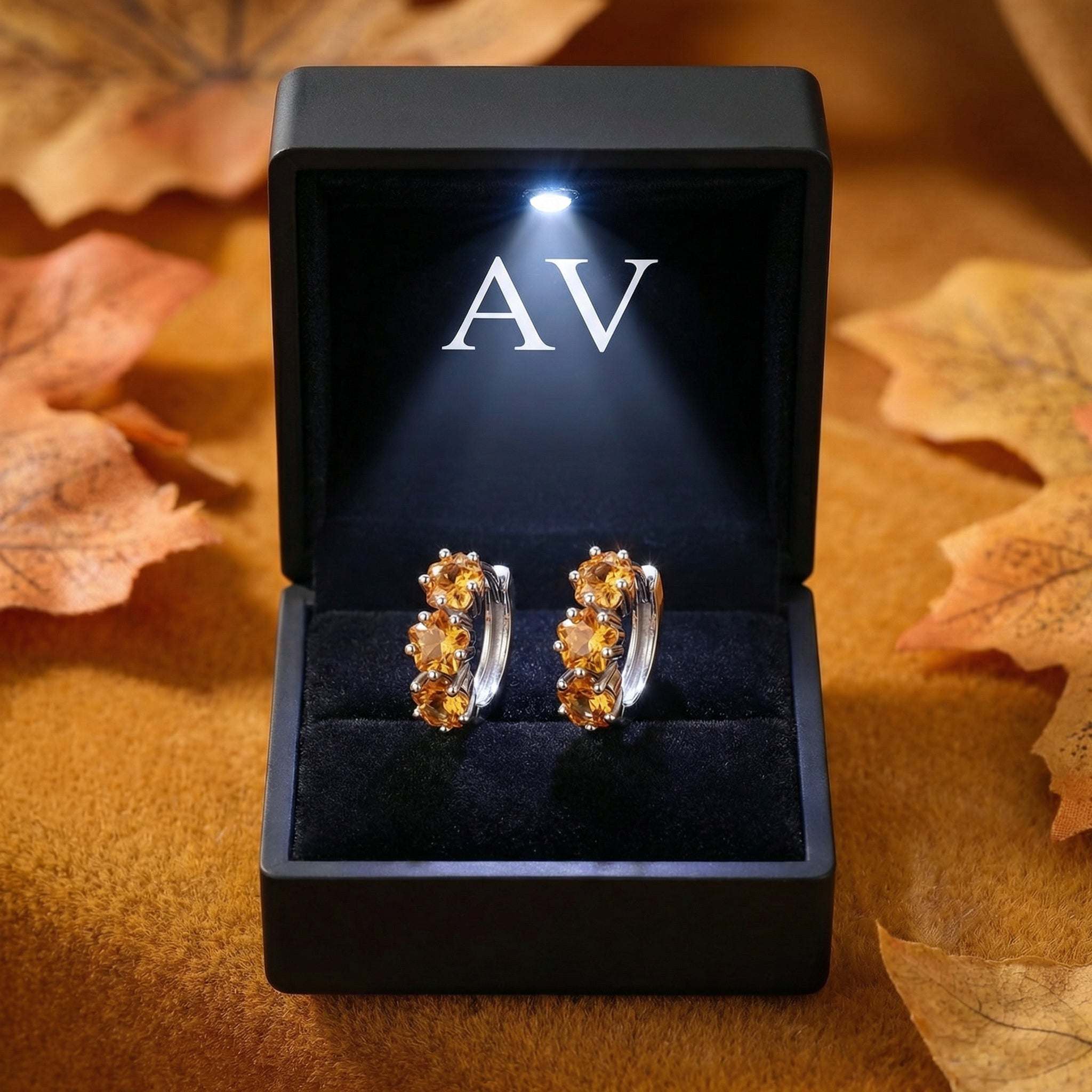 Aurellise sterling silver and simulated topaz huggie earrings in a black LED-lit jewelry presentation box.
