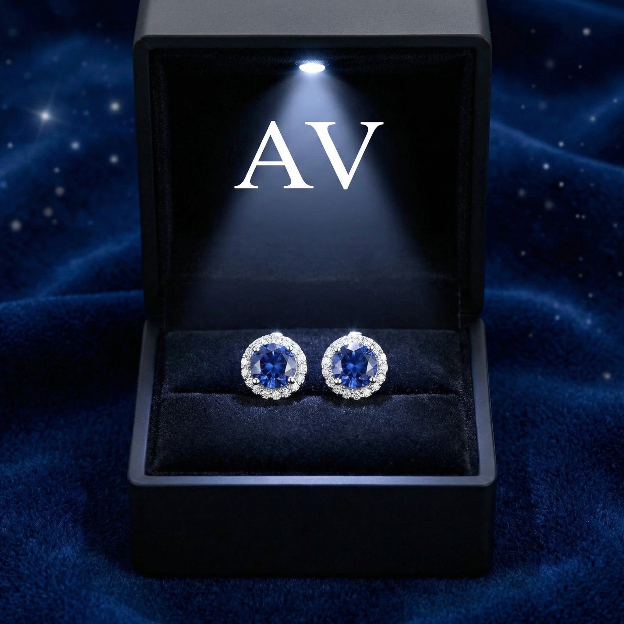 Round blue moissanite halo stud earrings in sterling silver inside a lighted black jewelry presentation box.