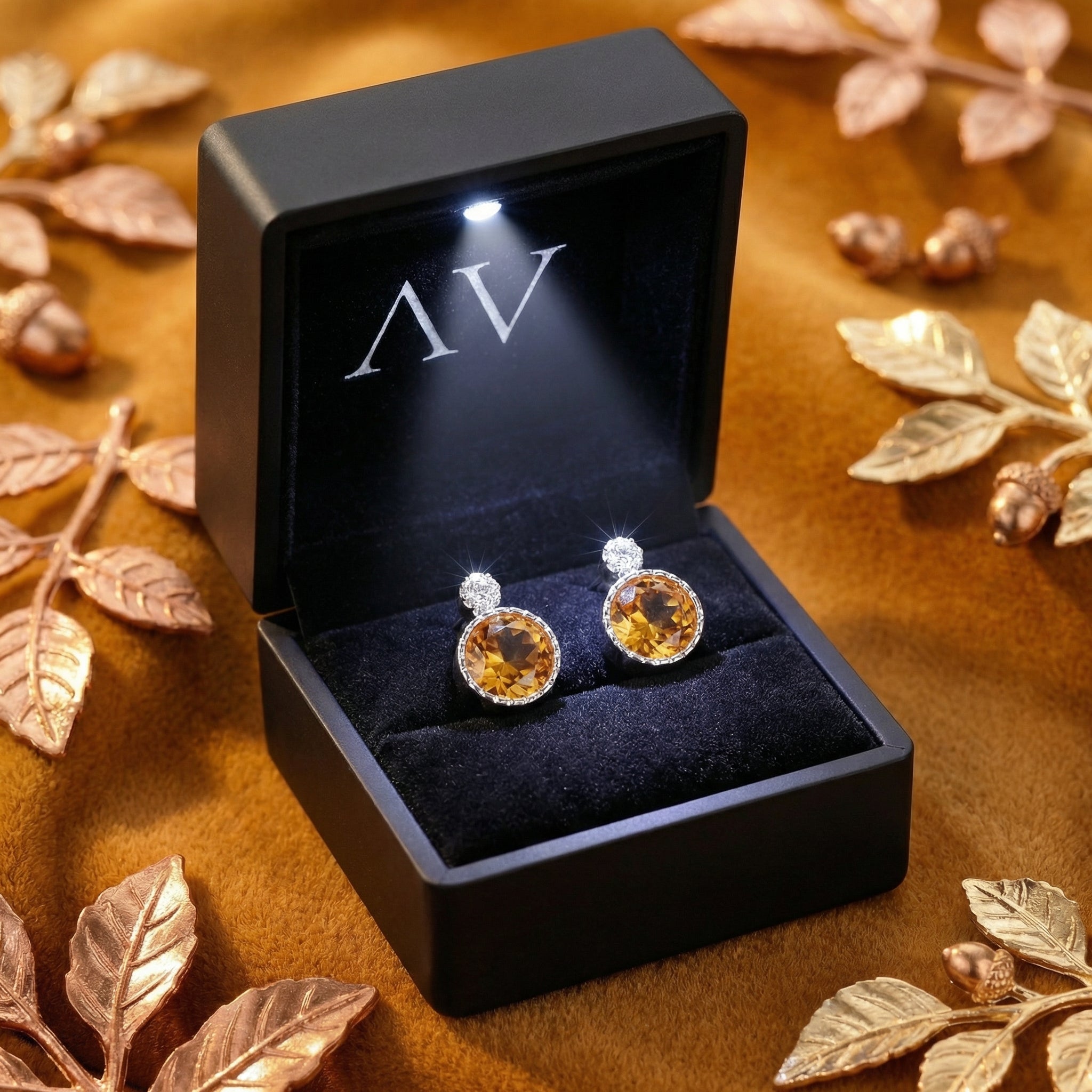 Round-cut simulated topaz earrings in a black LED-lighted gift box, styled with golden autumn leaves.
