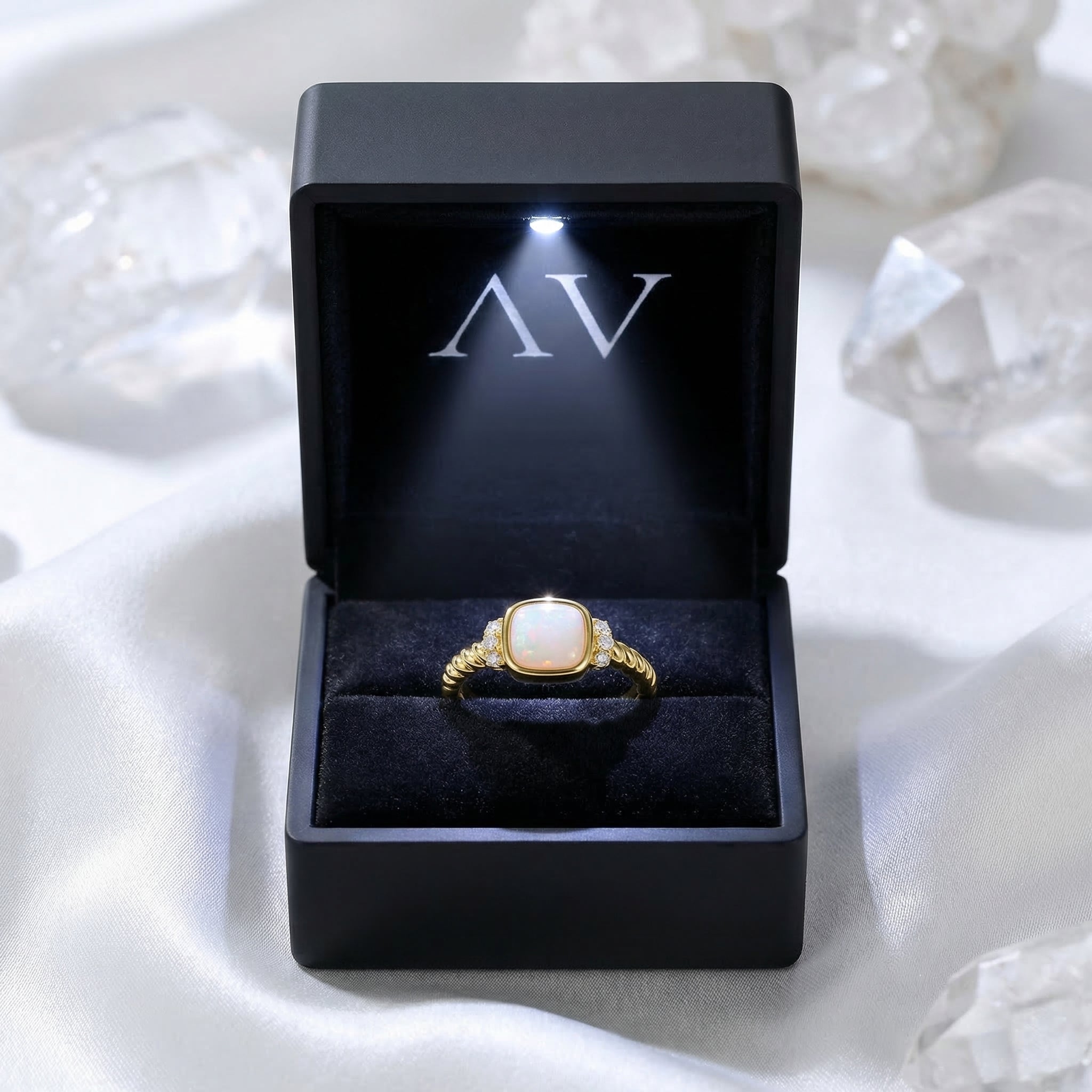 Cushion-cut white opal ring displayed in a black LED-lit jewelry box on a white silk surface.
