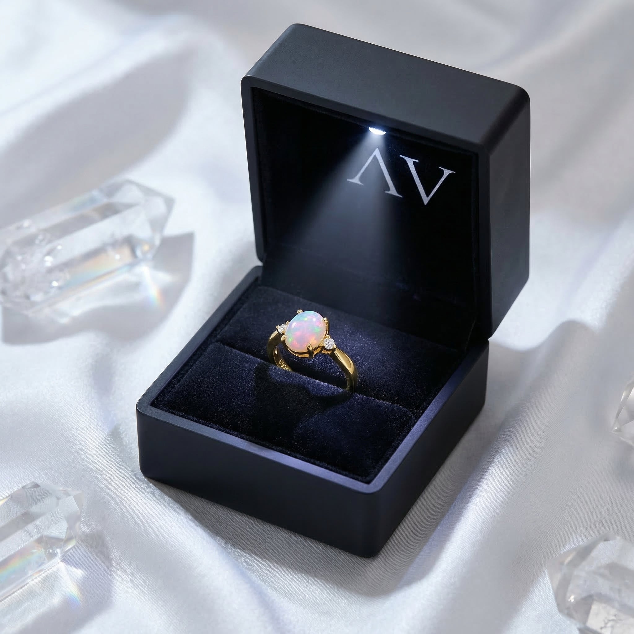 Gold-tone natural oval opal ring presented in a black LED-lit gift box on white silk with crystals.