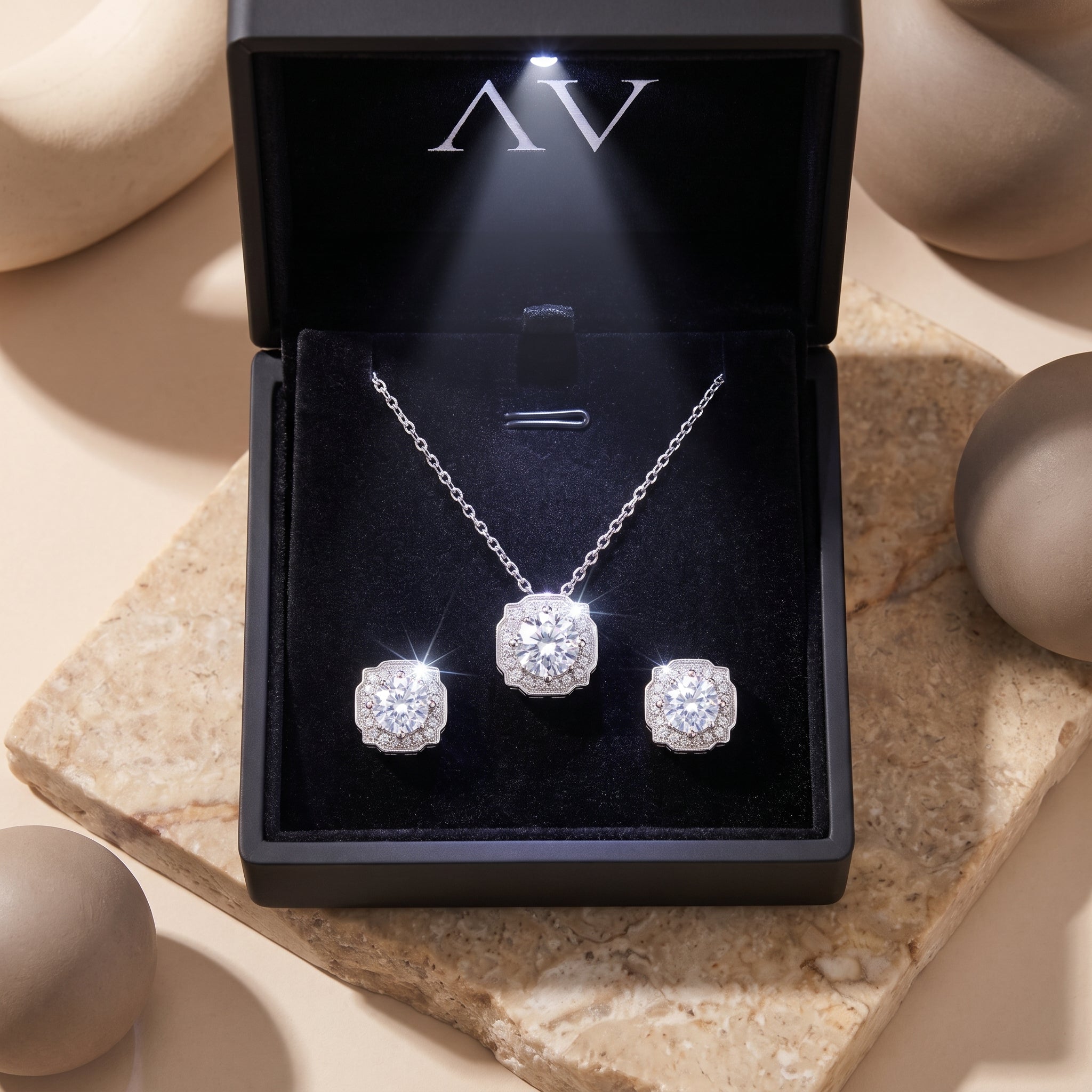 Aurestella moissanite necklace and earring set in a lighted black jewelry gift box on a stone surface.