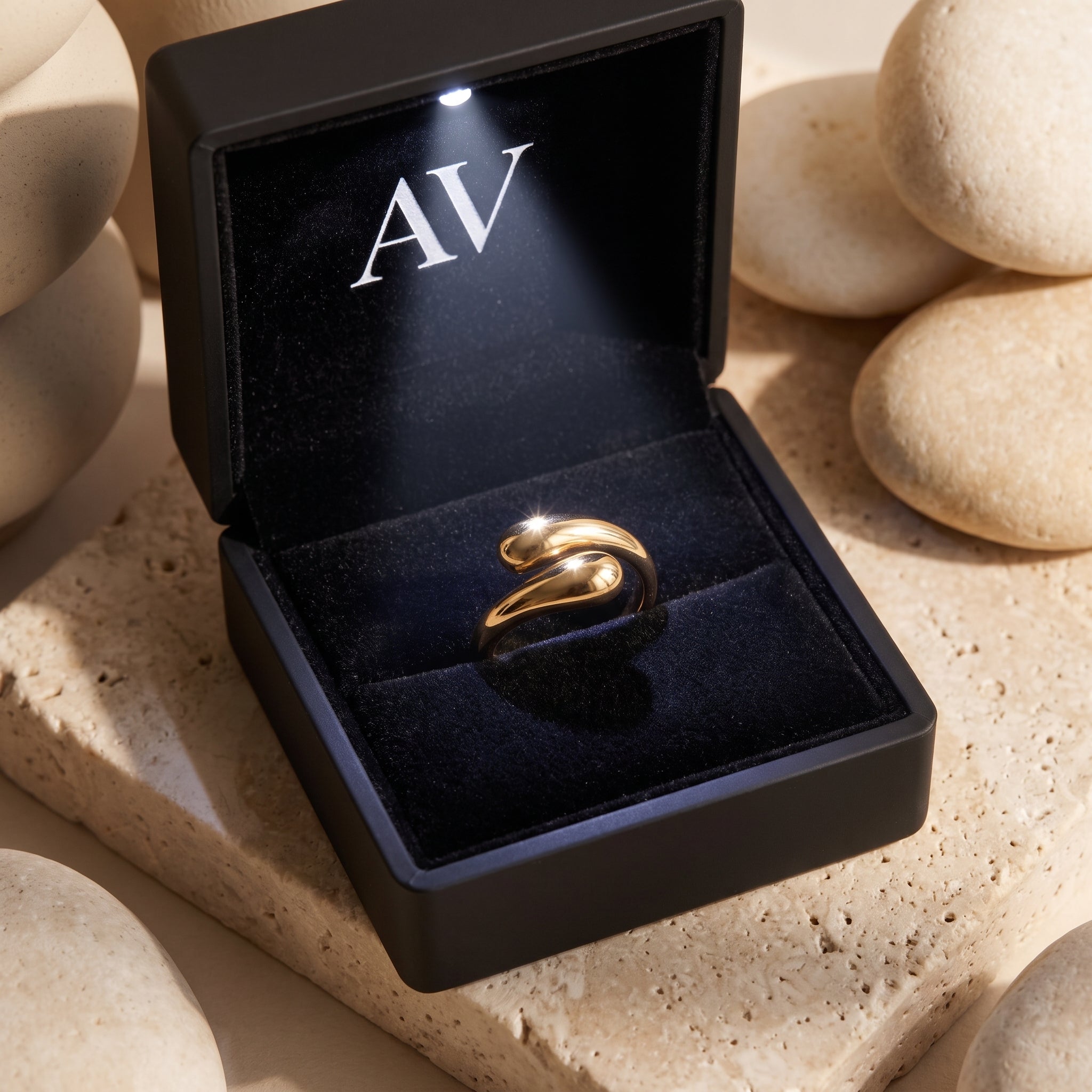 Gold bypass ring inside a black velvet jewelry box with an integrated LED light and AV branding.