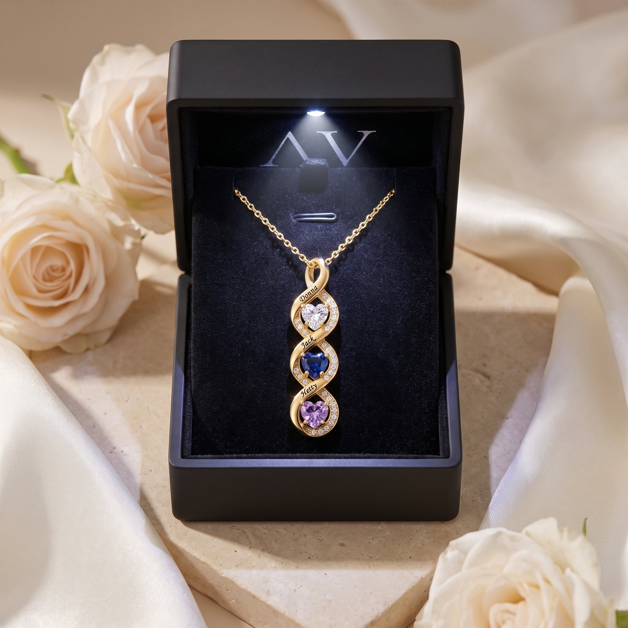 Gold infinity name necklace displayed in a luxury black LED-lit gift box with white roses.