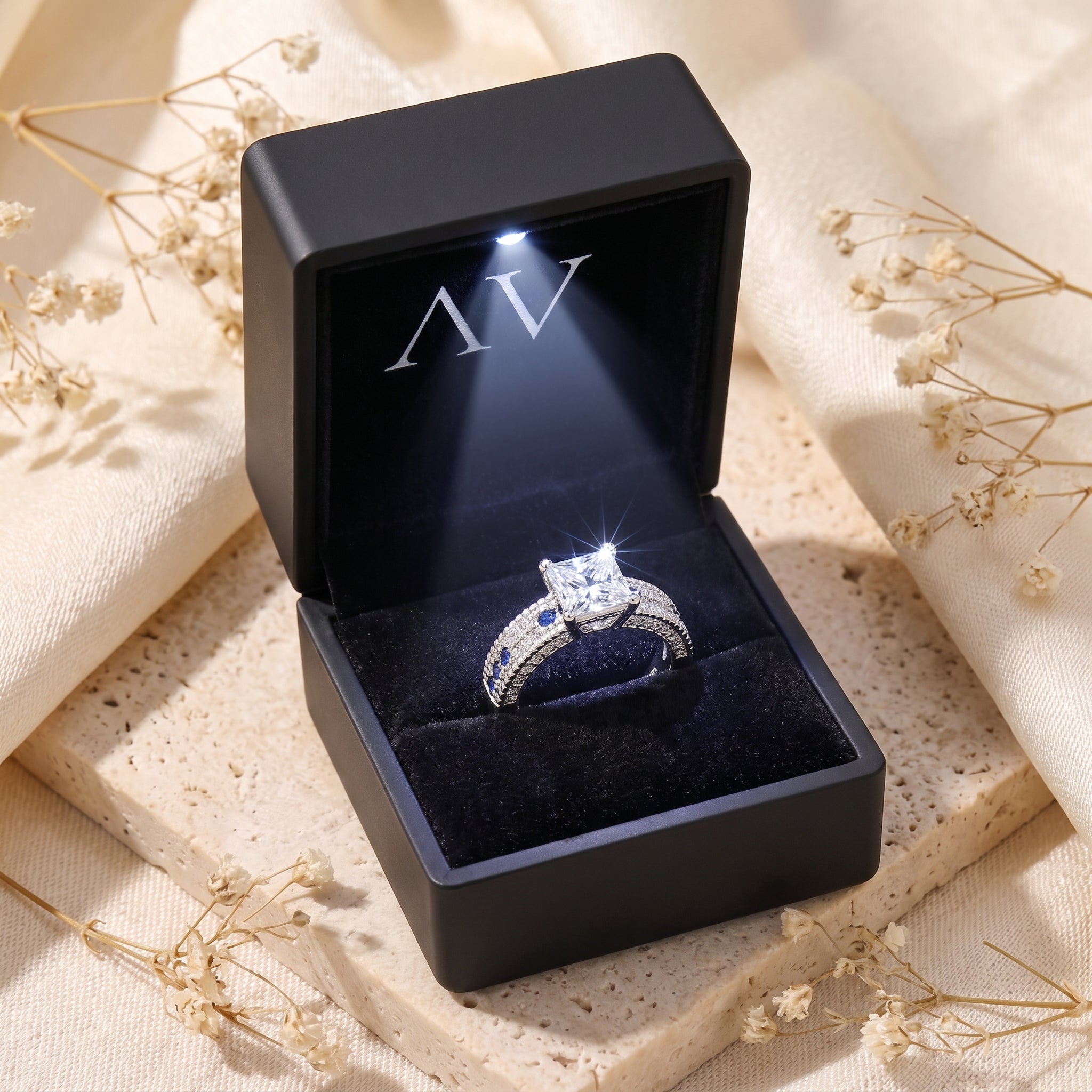 Princess-cut silver ring with blue accents inside a black LED-lit gift box.