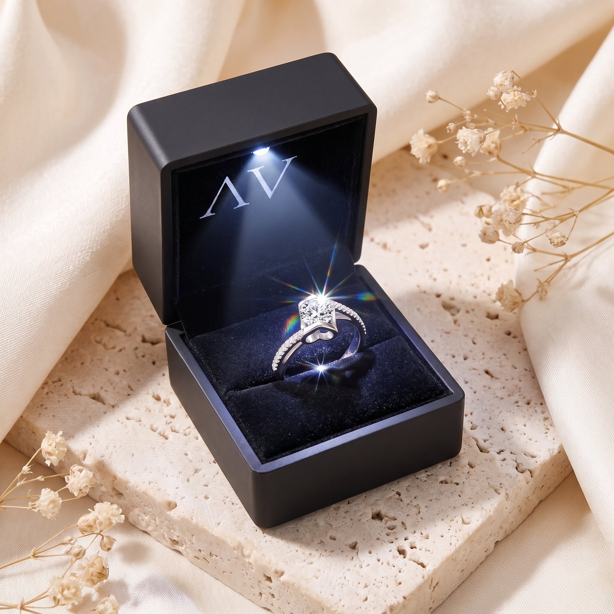 Silver round-cut solitaire ring presented in a black LED-lit jewelry gift box on a stone surface.