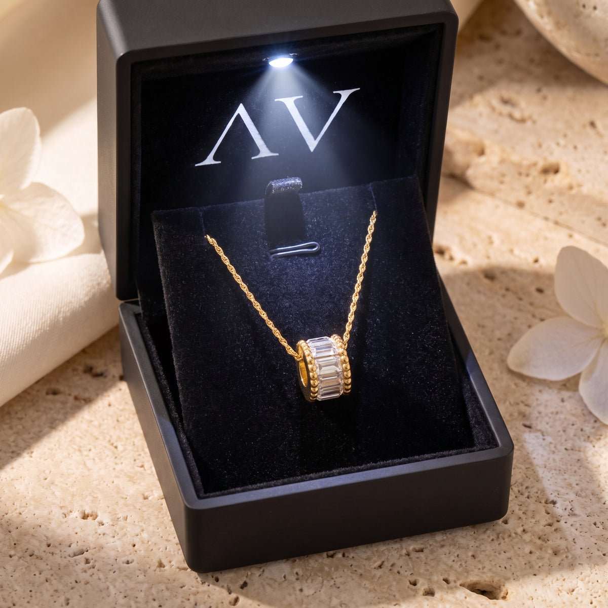 Gold Elyndelle necklace displayed in a black LED-lit jewelry gift box on a stone surface.
