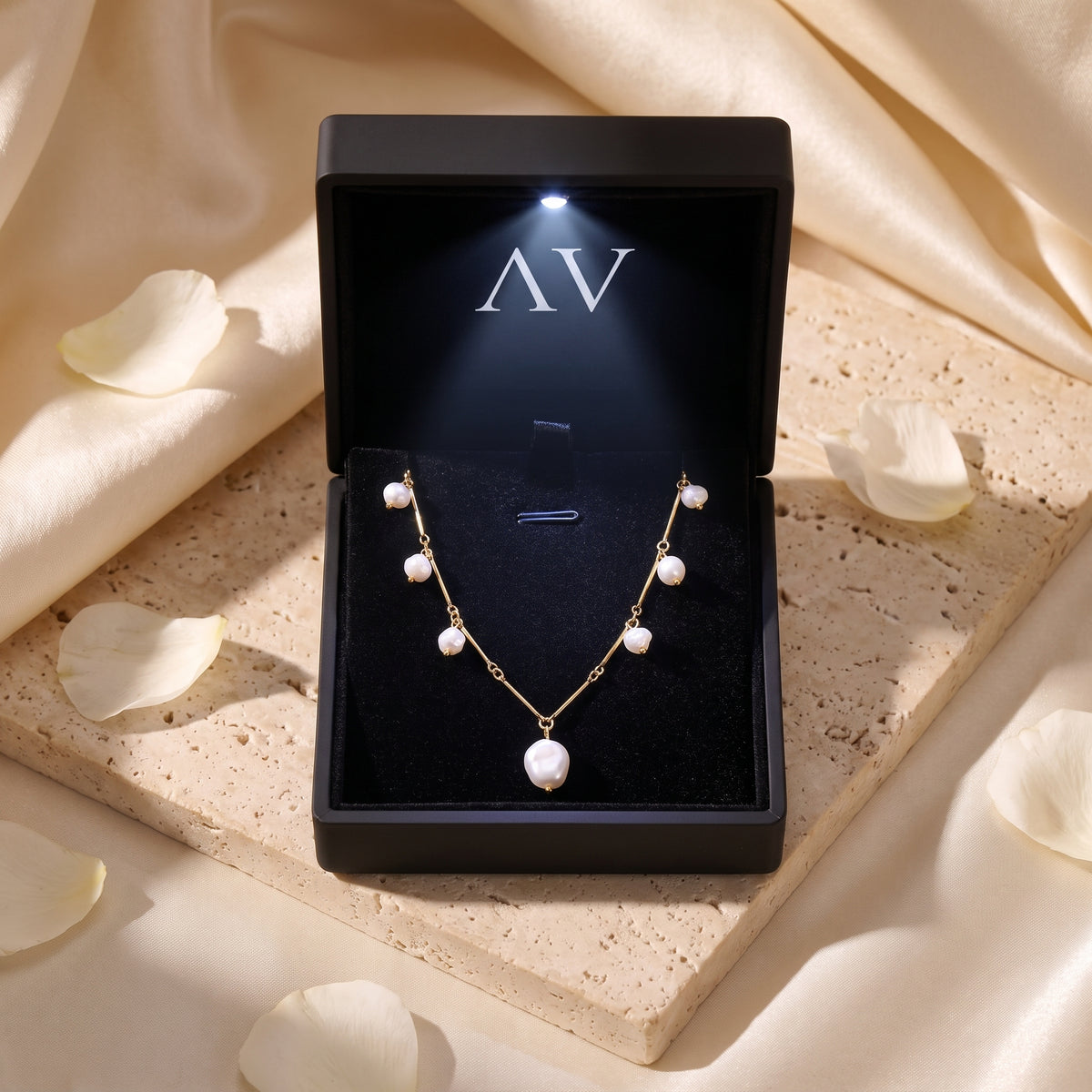 Gold finish baroque pearl necklace presented in a black LED-lit branded gift box on a stone surface.