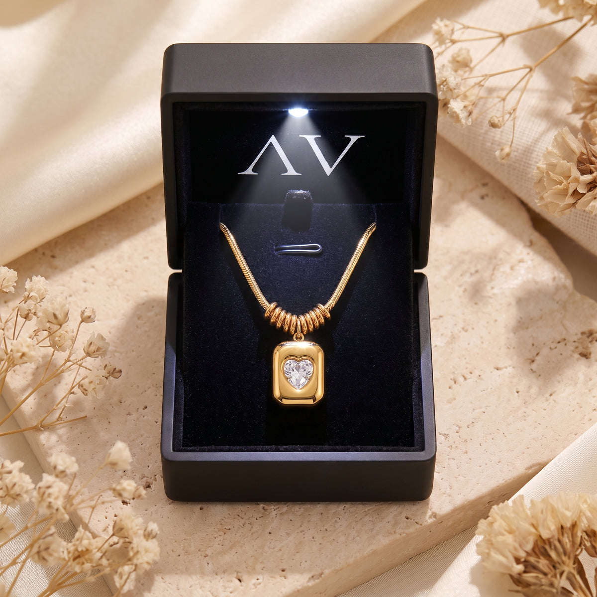 Gold Sophia Heart Necklace displayed in a black LED-lit jewelry box on a stone surface with flowers.